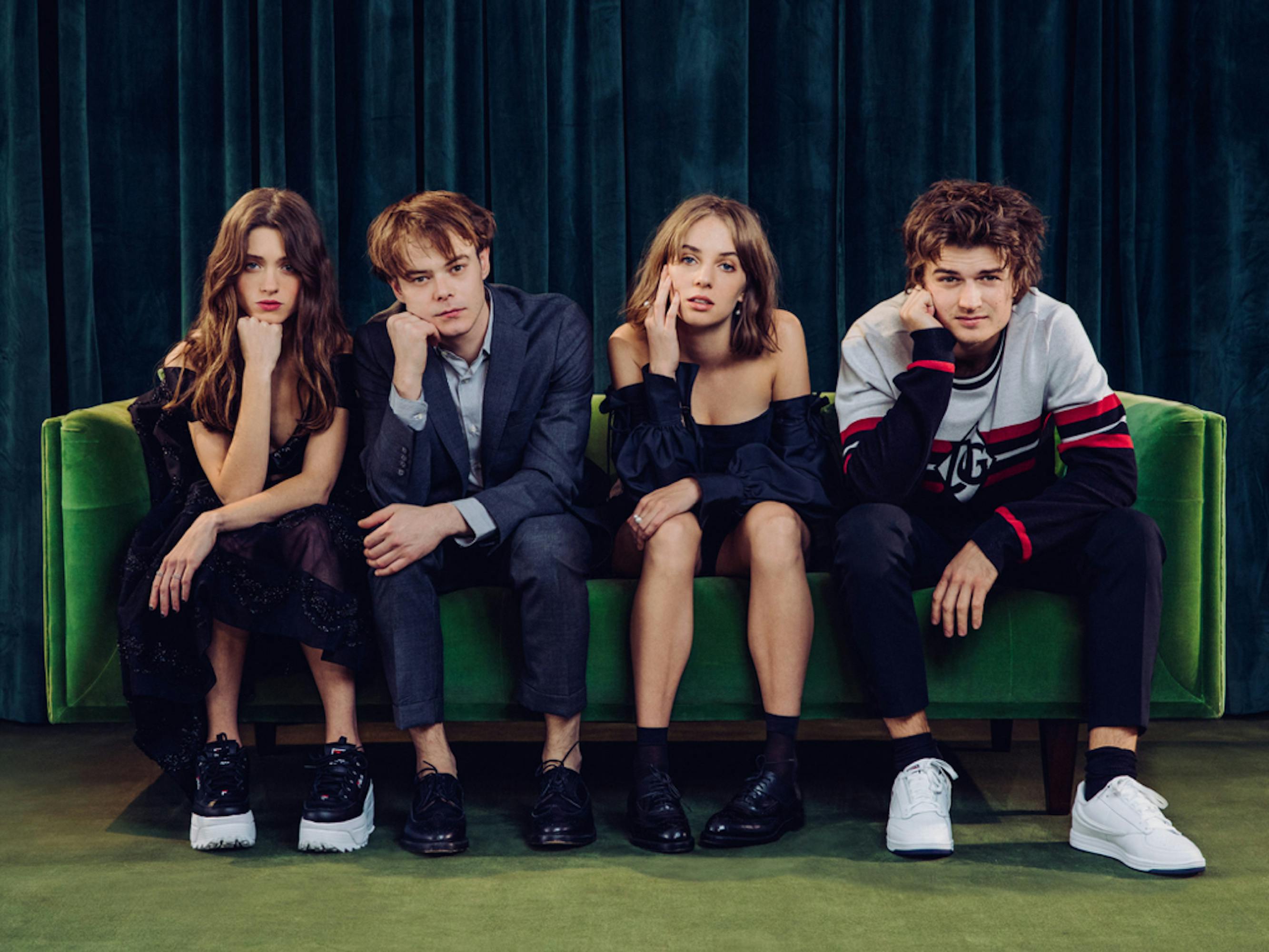 The young cast of Stranger Things sits on a green sofa and looks at the camera.