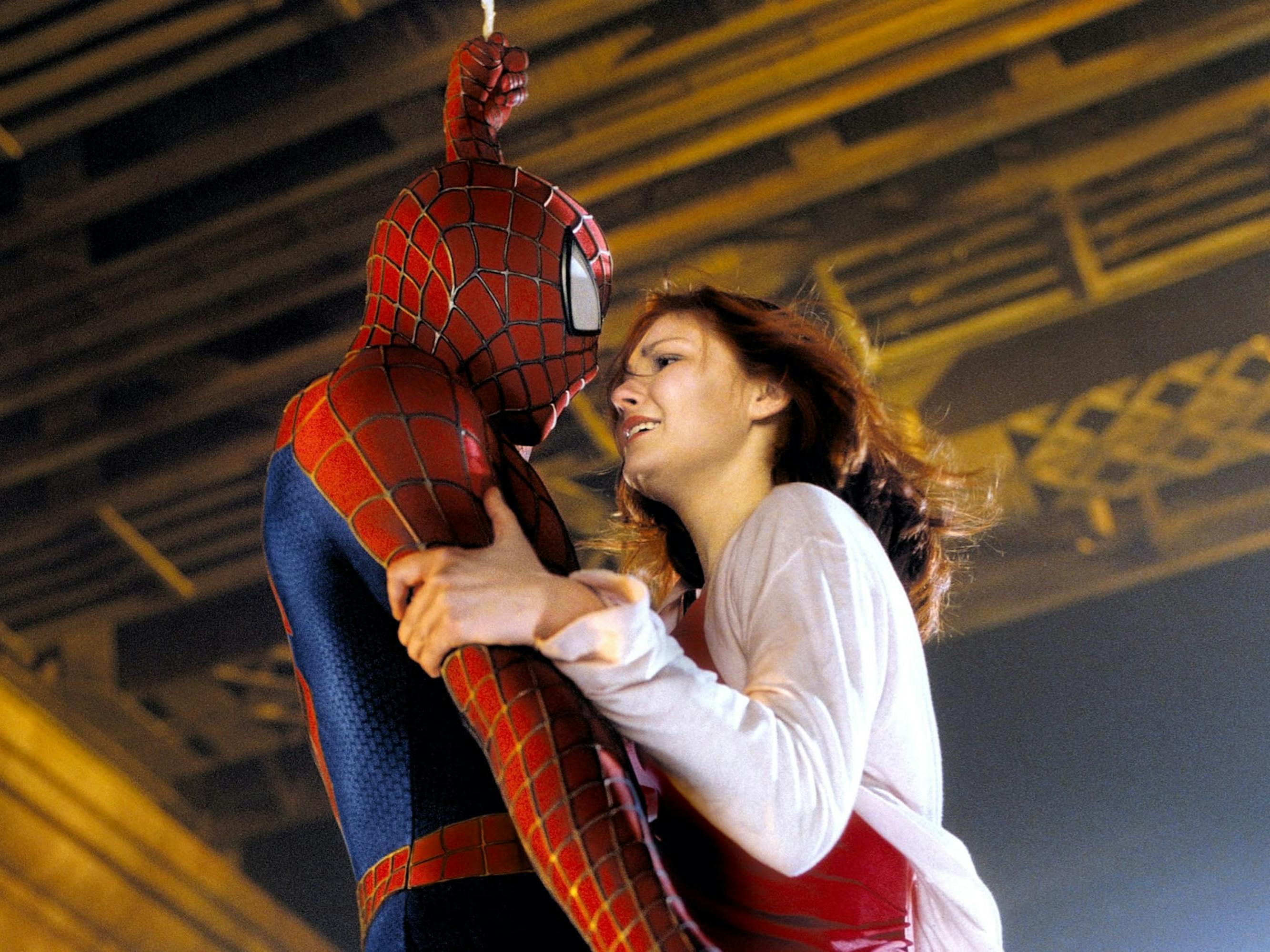 Spider-Man (Tobey Maguire) and Mary Jane Watson (Kirsten Dunst) stand together. Maguire wears his spidey suit, and Dunst wears a pink t-shirt.