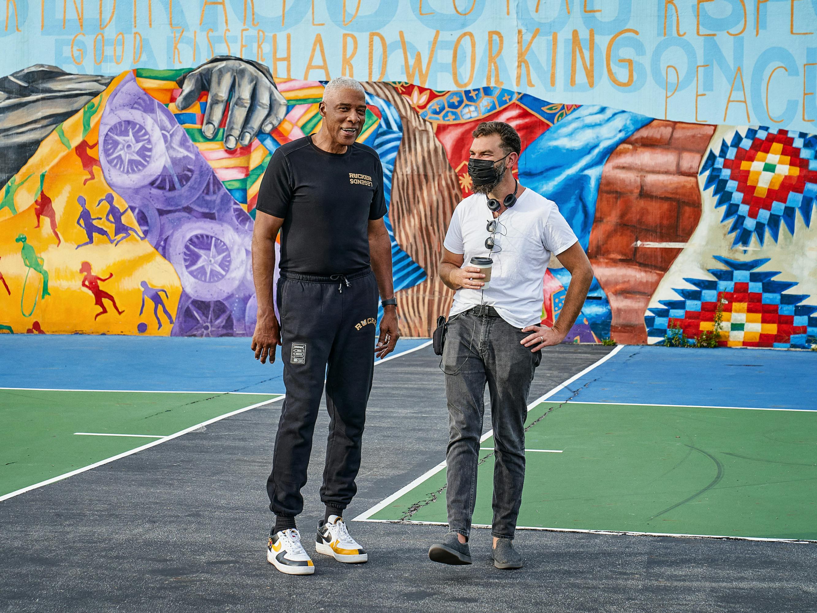Dr. J (Julius Erving) and Jeremiah Zagar stand on an outdoor basketball court against a colorful mural.