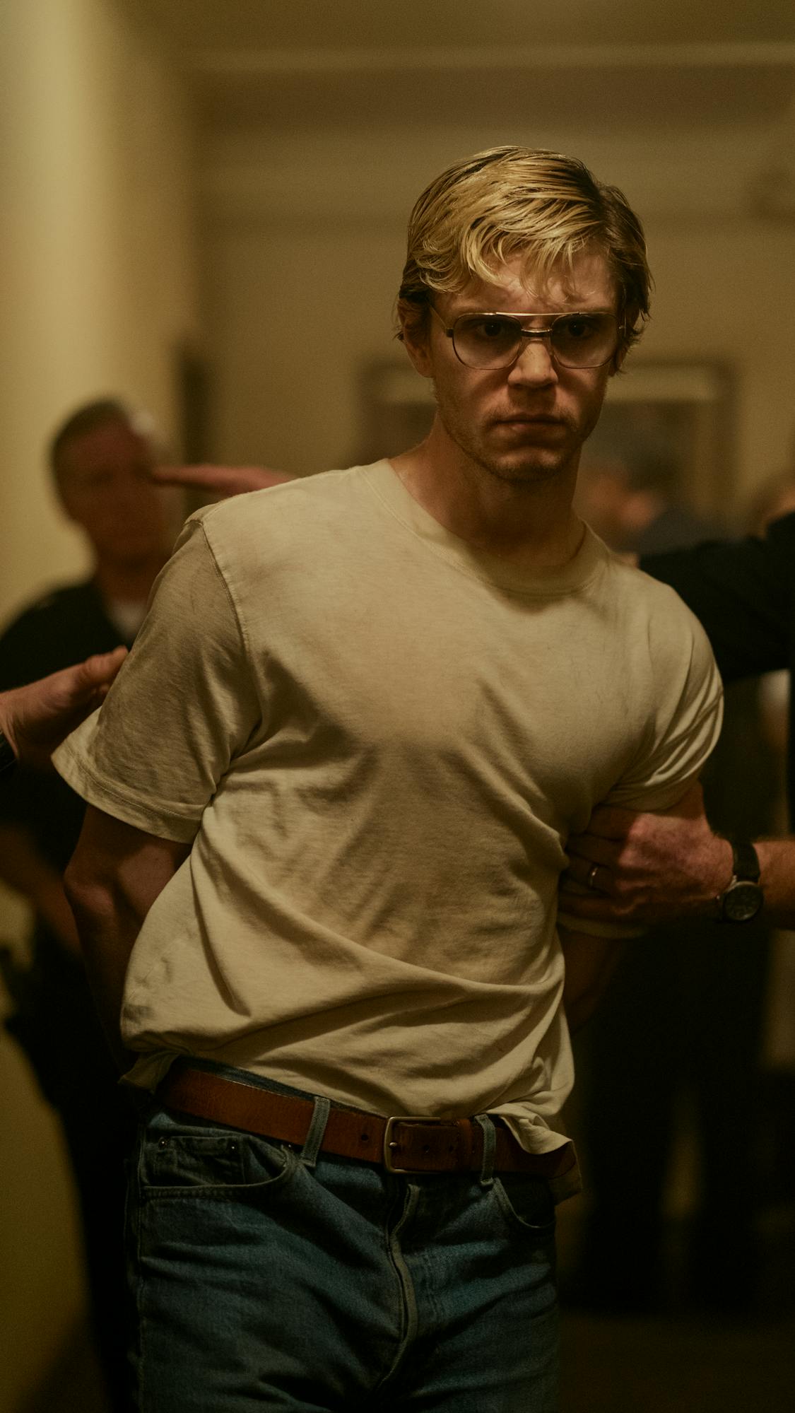 Jeffrey Dahmer (Evan Peters) wears a white top and is escorted by police officers.