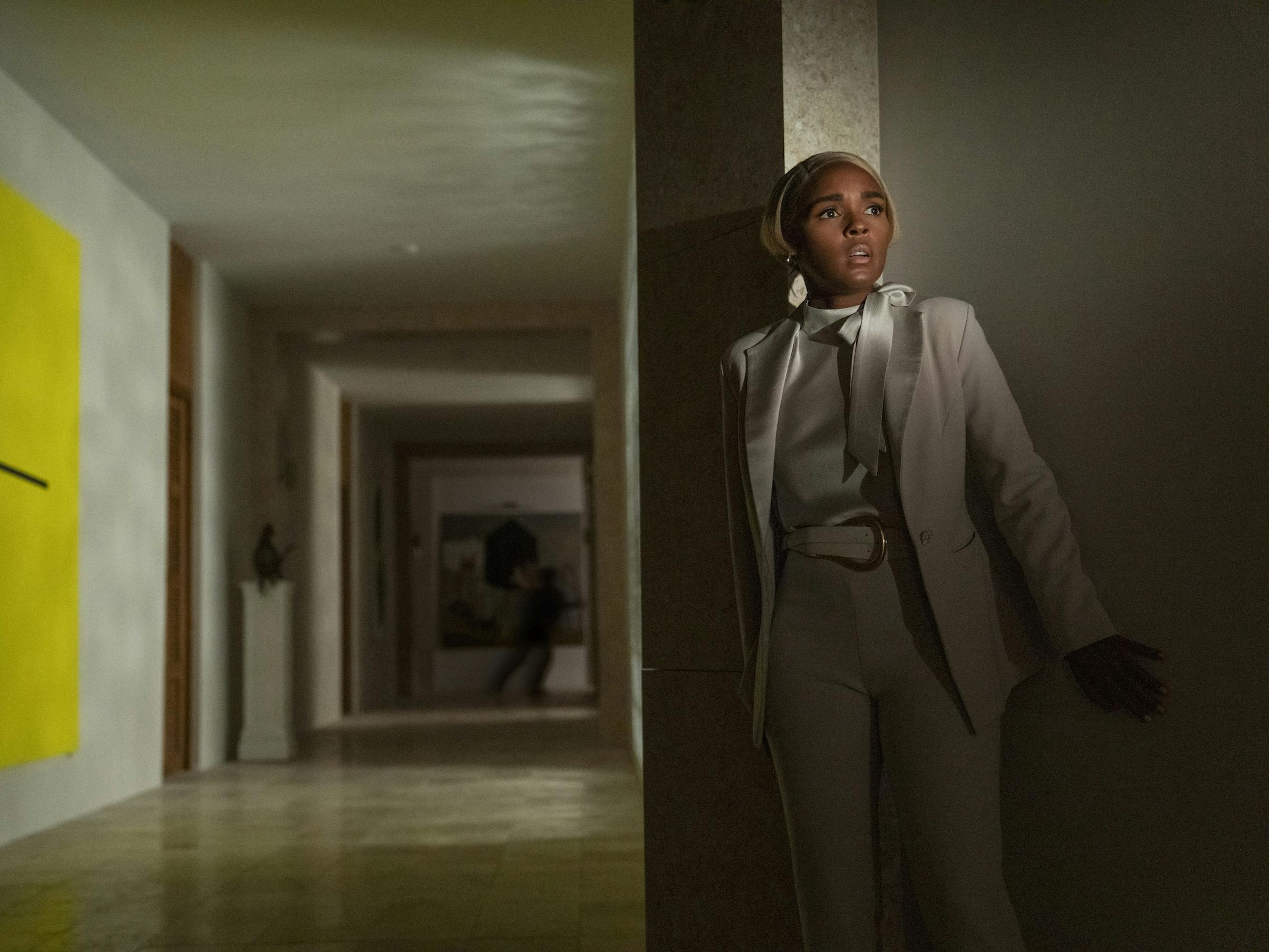 Andi Brand (Janelle Monáe) crouches behind a wall in a darkened hallway.