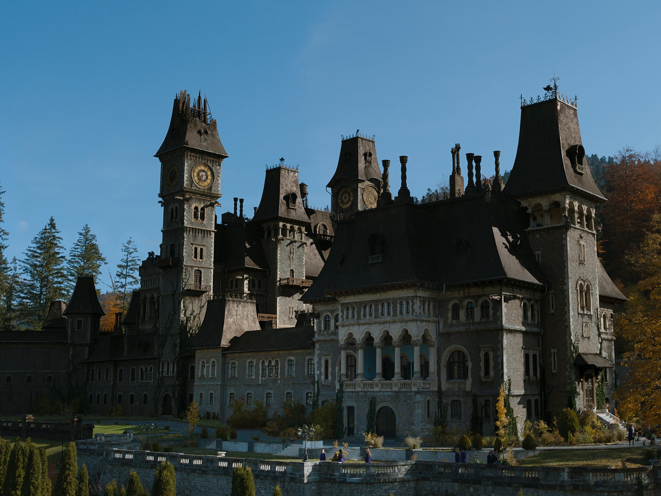 Nevermore Academy looms large against an autumnal forest and a bright blue sky.