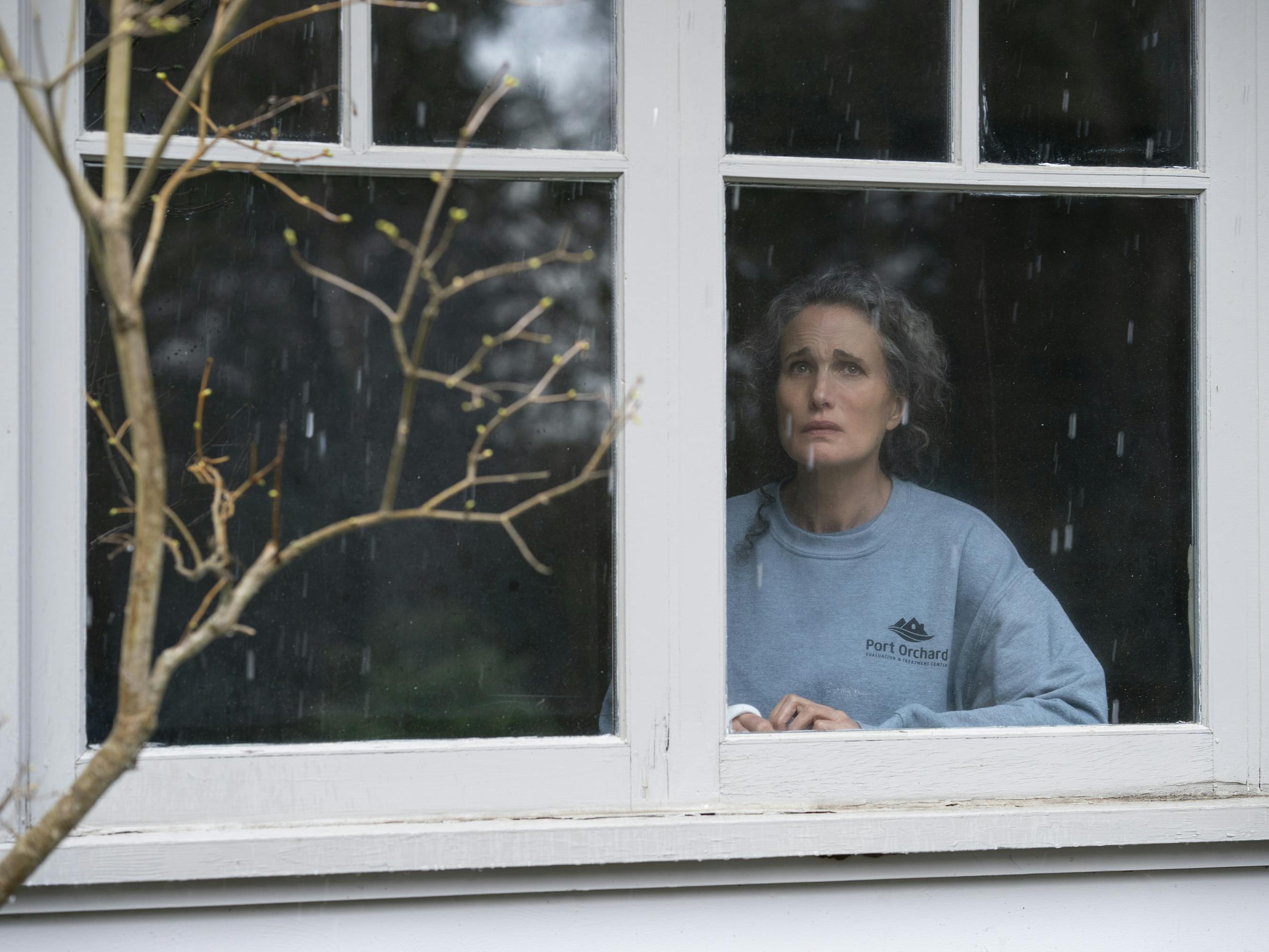 Andie MacDowell in Maid wears a grey sweatshirt and looks out the window.