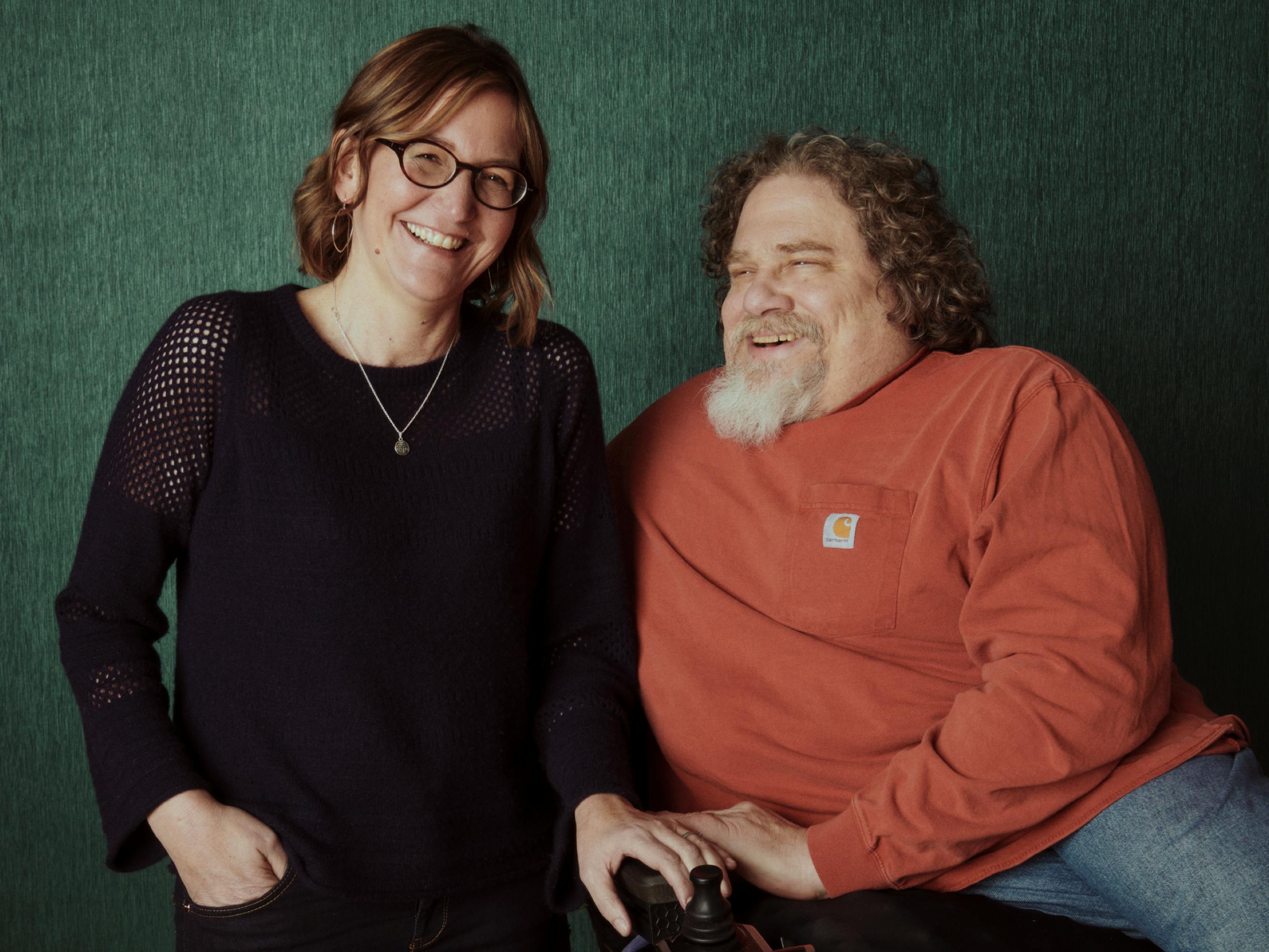 Crip Camp co-directors Nicole Newnham and Jim LeBrecht pose, laughing, in front of a green backdrop.