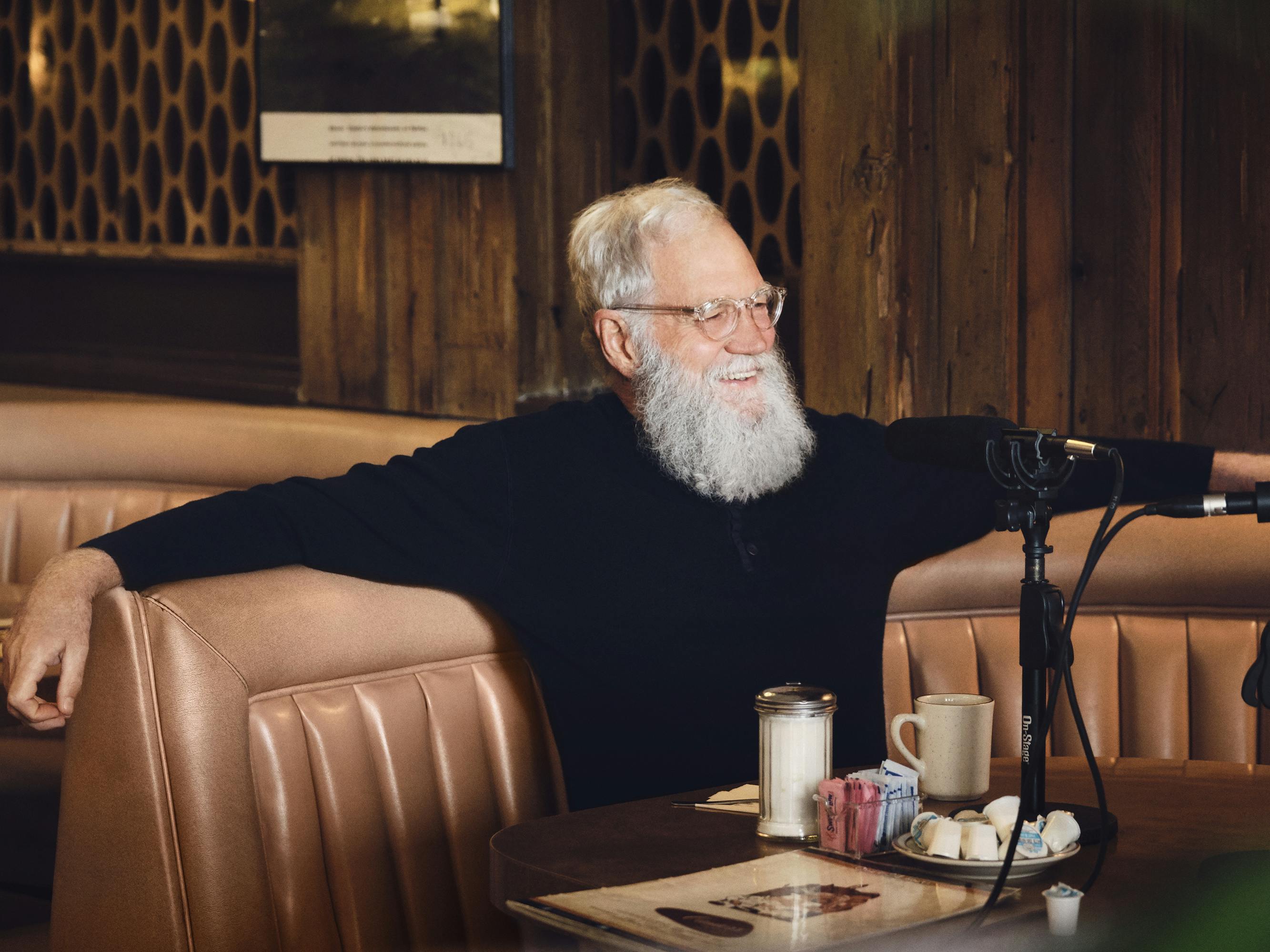 David Letterman wears a dark sweater and sits in a brown leather booth.