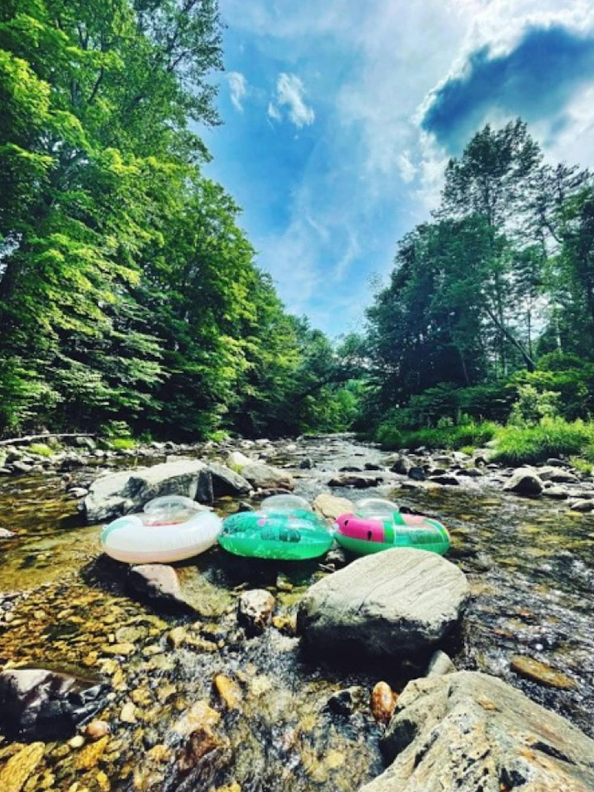 Saxtons River scene, with three inflatable tubes, green trees, a blue sky, and lots of rocks. It is the picture of a happy summer day!
