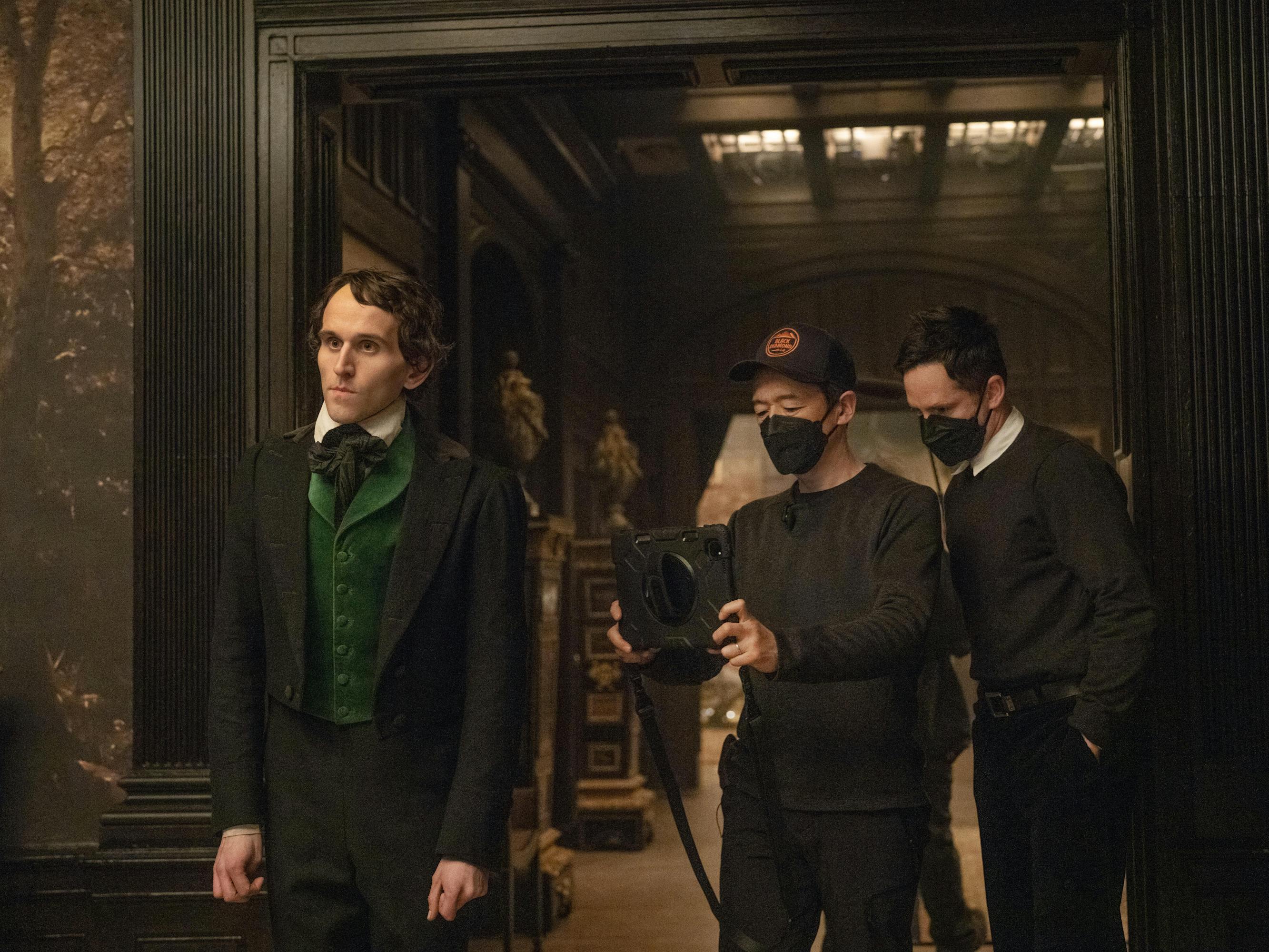 Edgar Allen Poe (Harry Melling) wears a green vest and dark blazer. Cinematographer Masanobu Takayanagi stands next to writer-director Scott Cooper in a doorway.