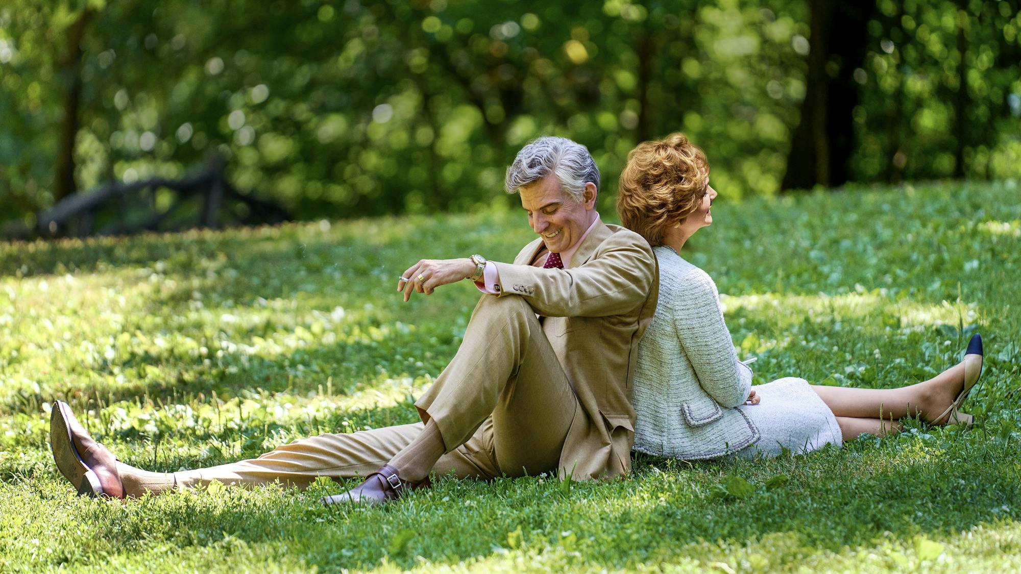 Leonard Bernstein (Bradley Cooper) and Felicia Montealegre Cohn Bernstein (Carey Mulligan) sit back to back in a green field. 