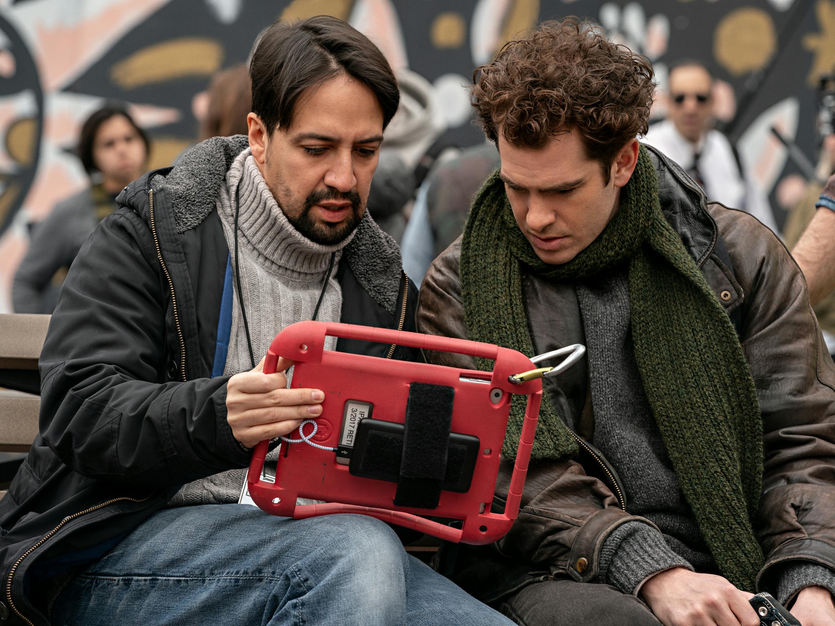 Lin-Manuel Miranda and Andrew Garfield look at footage on a small red ipad. 