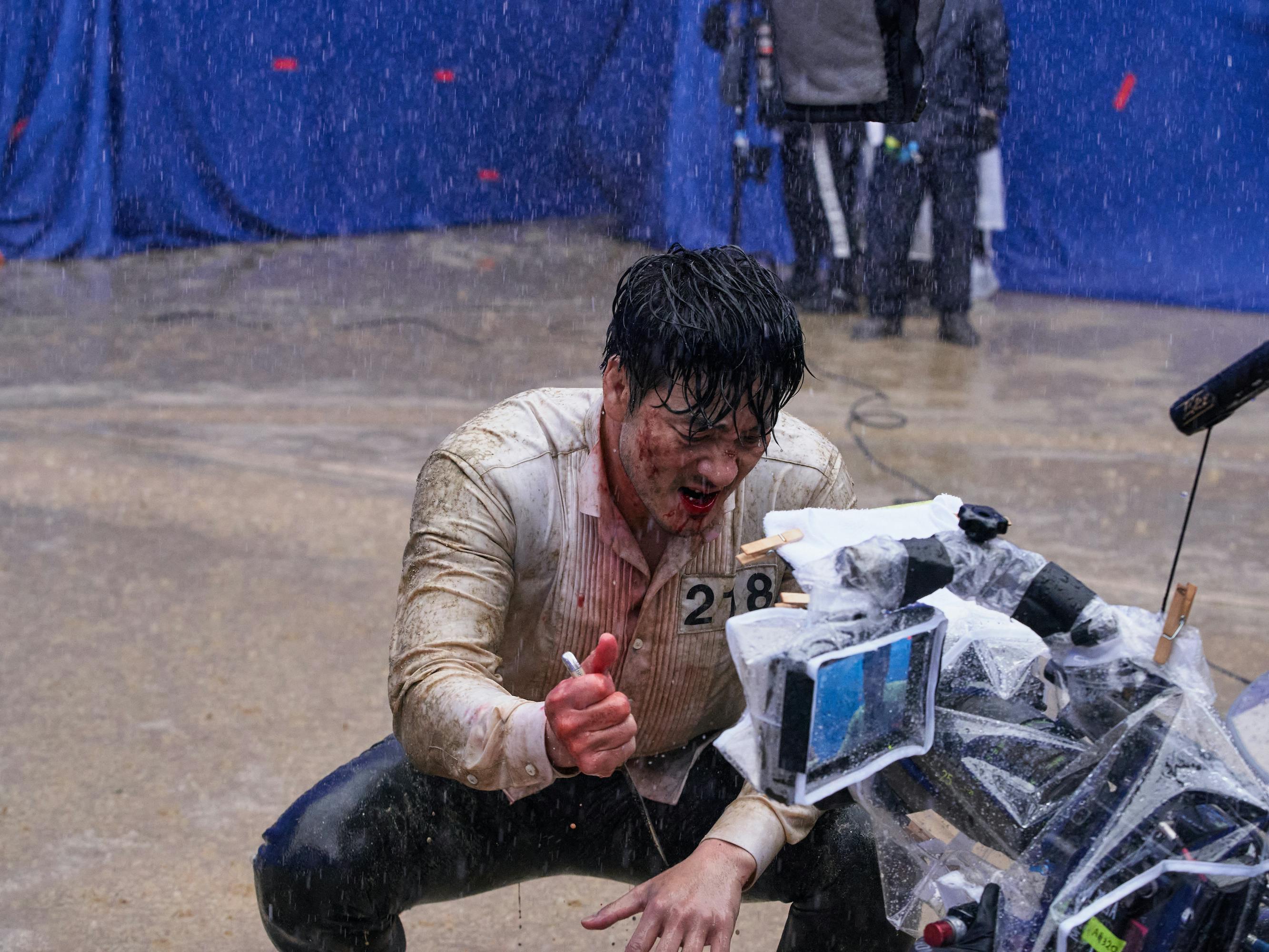 Cho Sang-woo (Park Hae-soo) squints in the rain. He faces a camera rig and looks wet and bloody.