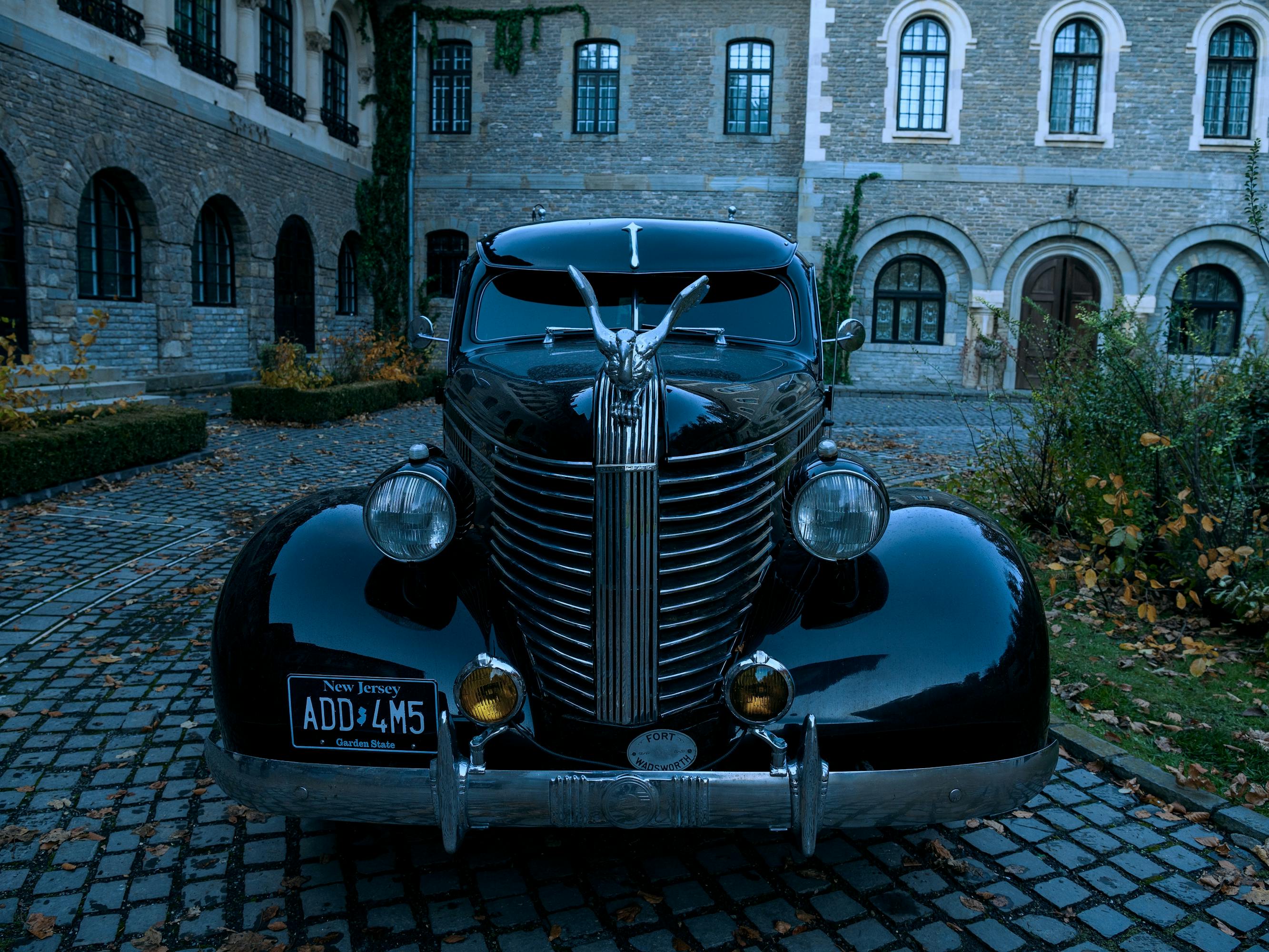 The Addams family limo sits in Nevermore's driveway. The exterior is glossy black.