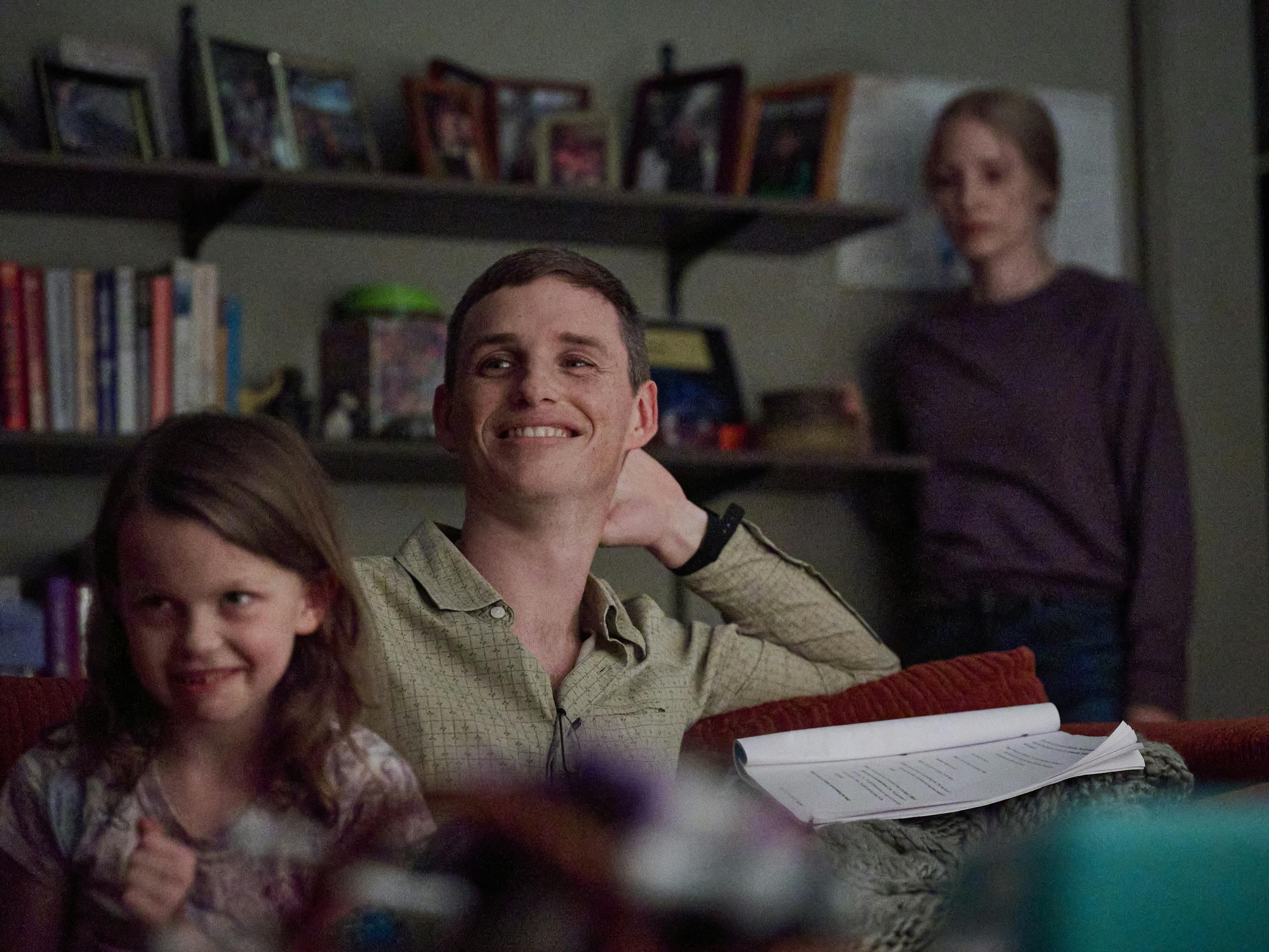 Maya Loughren (Devyn McDowell), Charles Cullen (Eddie Redmayne), and Amy Loughren (Jessica Chastain) sit together in a living room. On the wall are hanging shelves with books.