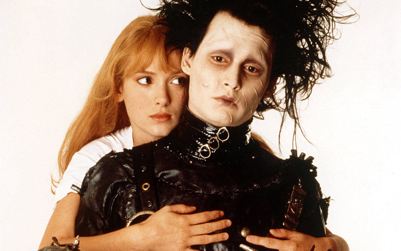 Kim (Winona Ryder) stands behind and hugs Edward Scissorhands (Johnny Depp).