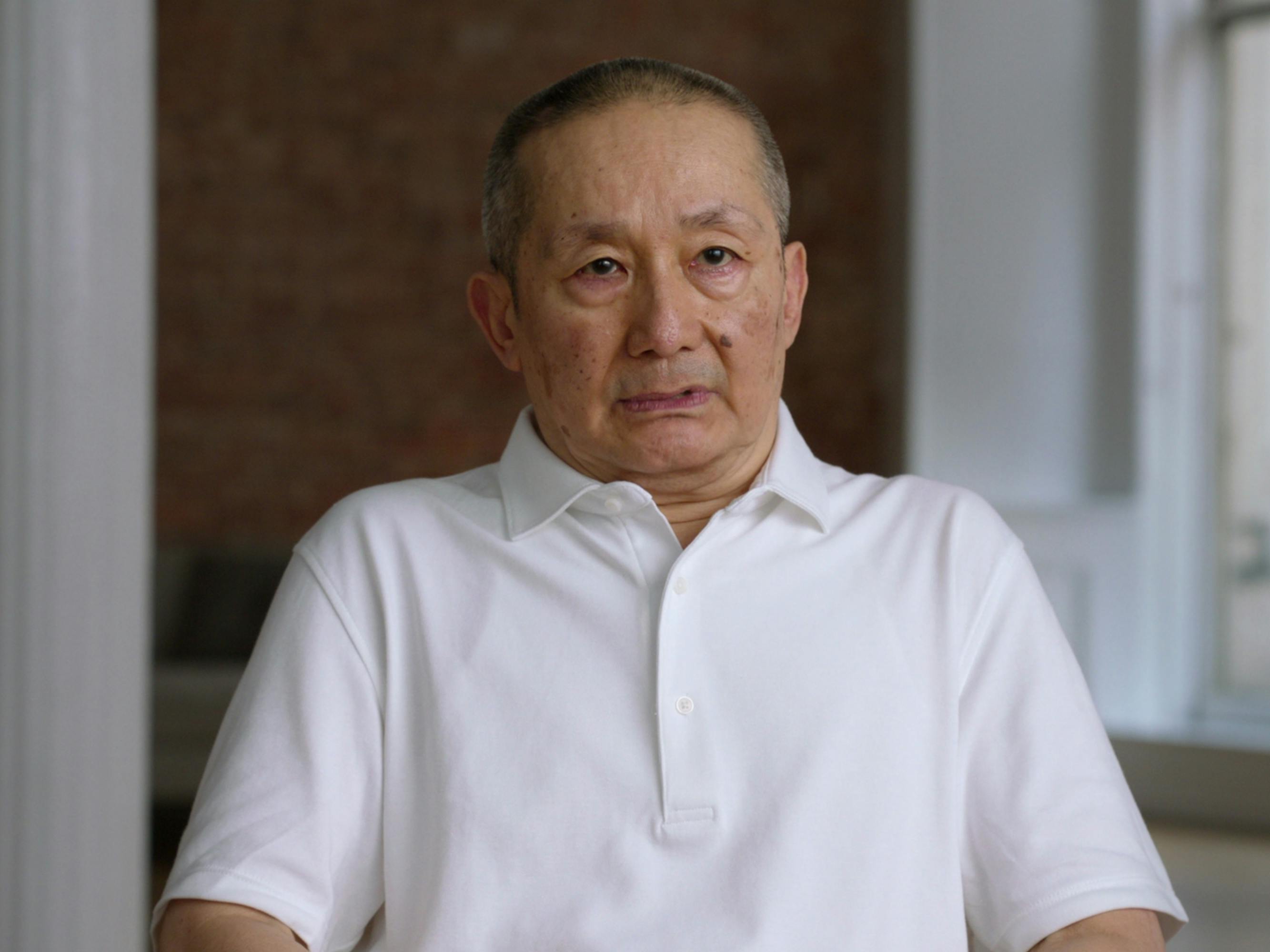 Benjamin Liu wears a white polo and sits in a brick-walled room.