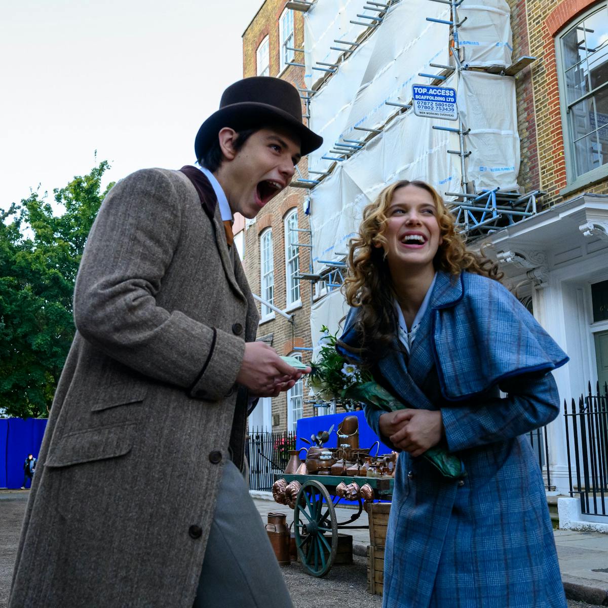 Tewkesbury (Louis Partridge) and Enola Holmes (Millie Bobby Brown) laugh in the street.
