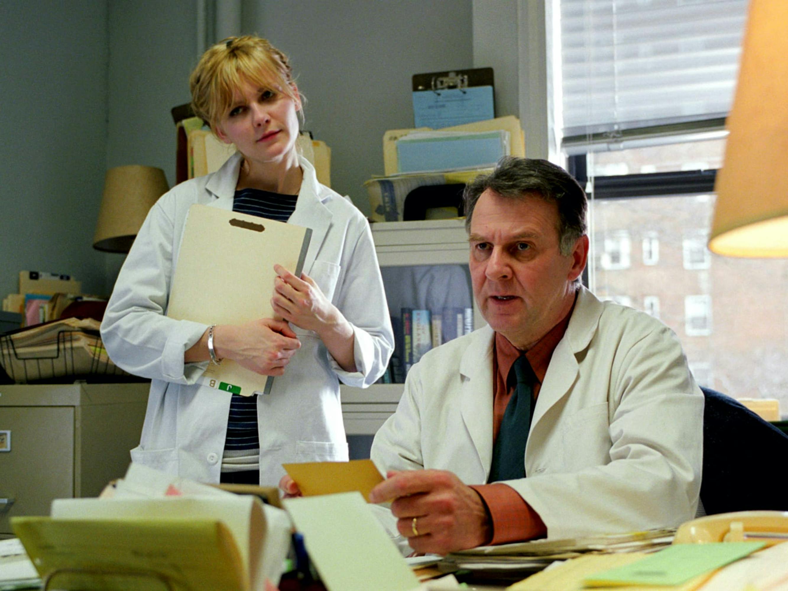 Mary (Kirsten Dunst) and Dr. Mierzwiak (Tom Wilkinson) stand in an office surrounded by filing cabinets and folders. They both wear white jackets.