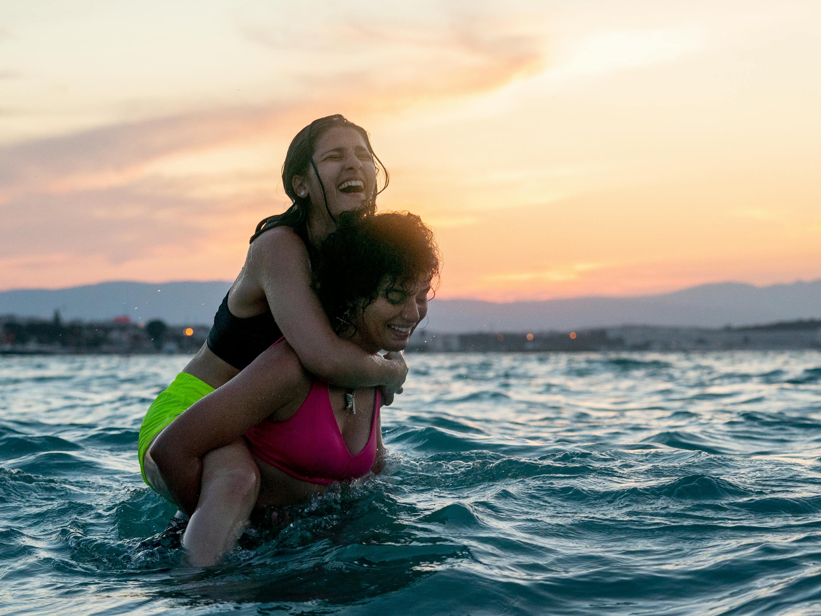 Yusra and Sarah Mardini laugh in this sunset-lit beach scene.