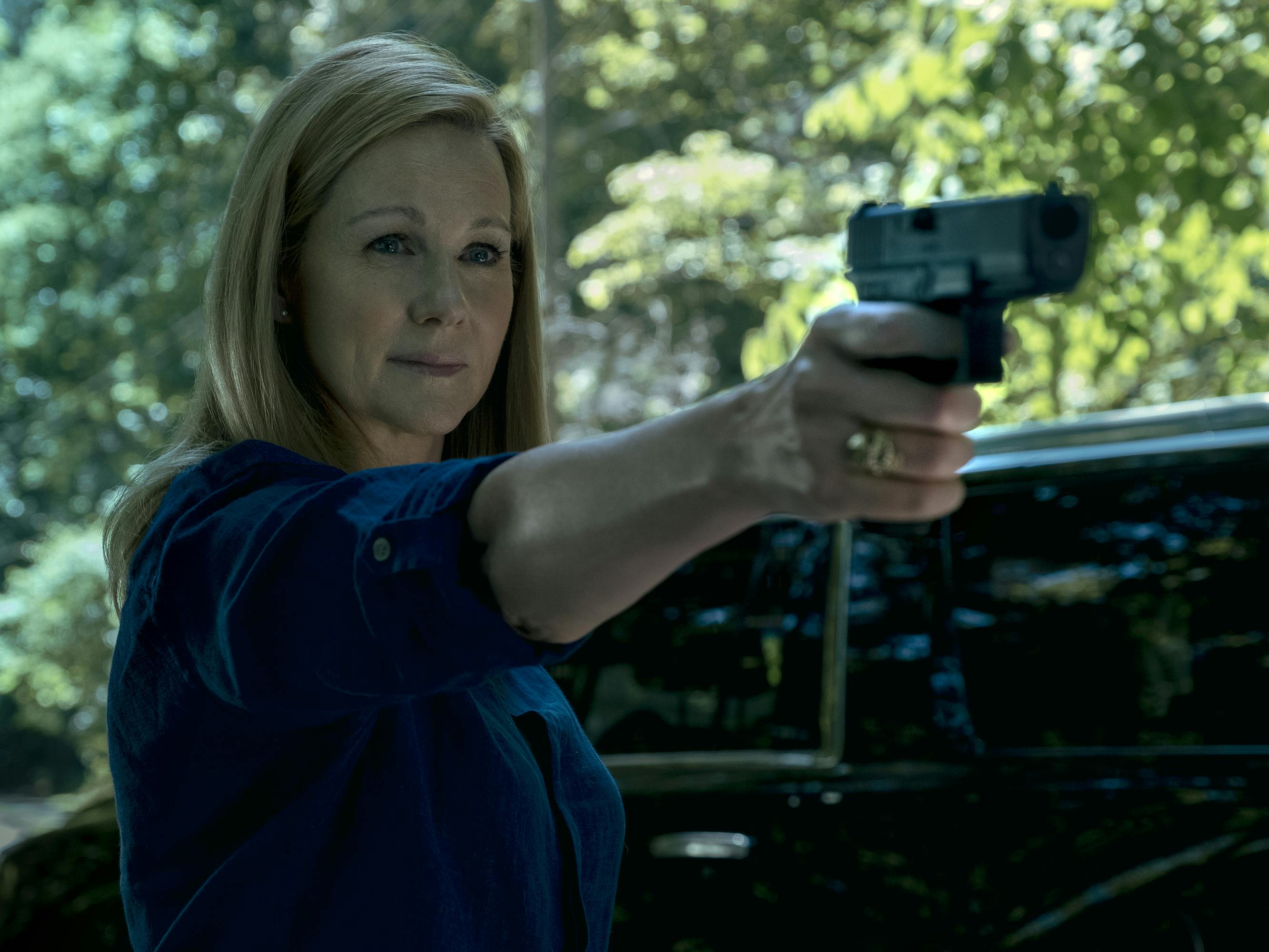 Wendy Bryde (Laura Linney) holds a gun at someone off screen in this sunlight dappled shot.