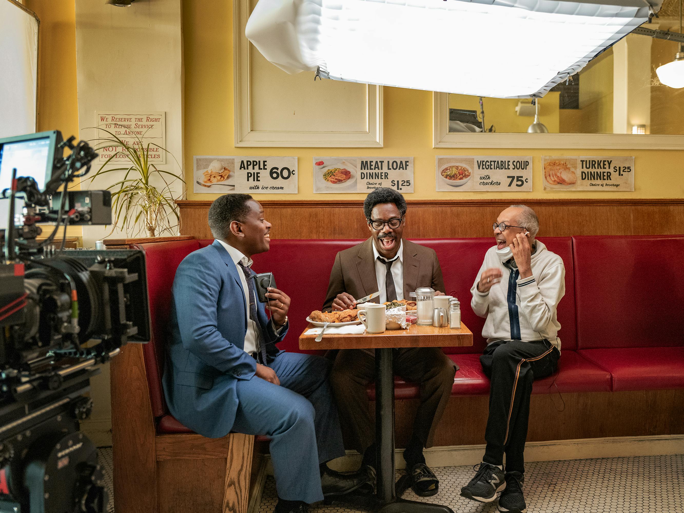 Behind the scenes with Aml Ameen, Colman Domingo, and George C. Wolfe at a diner with red booths.
