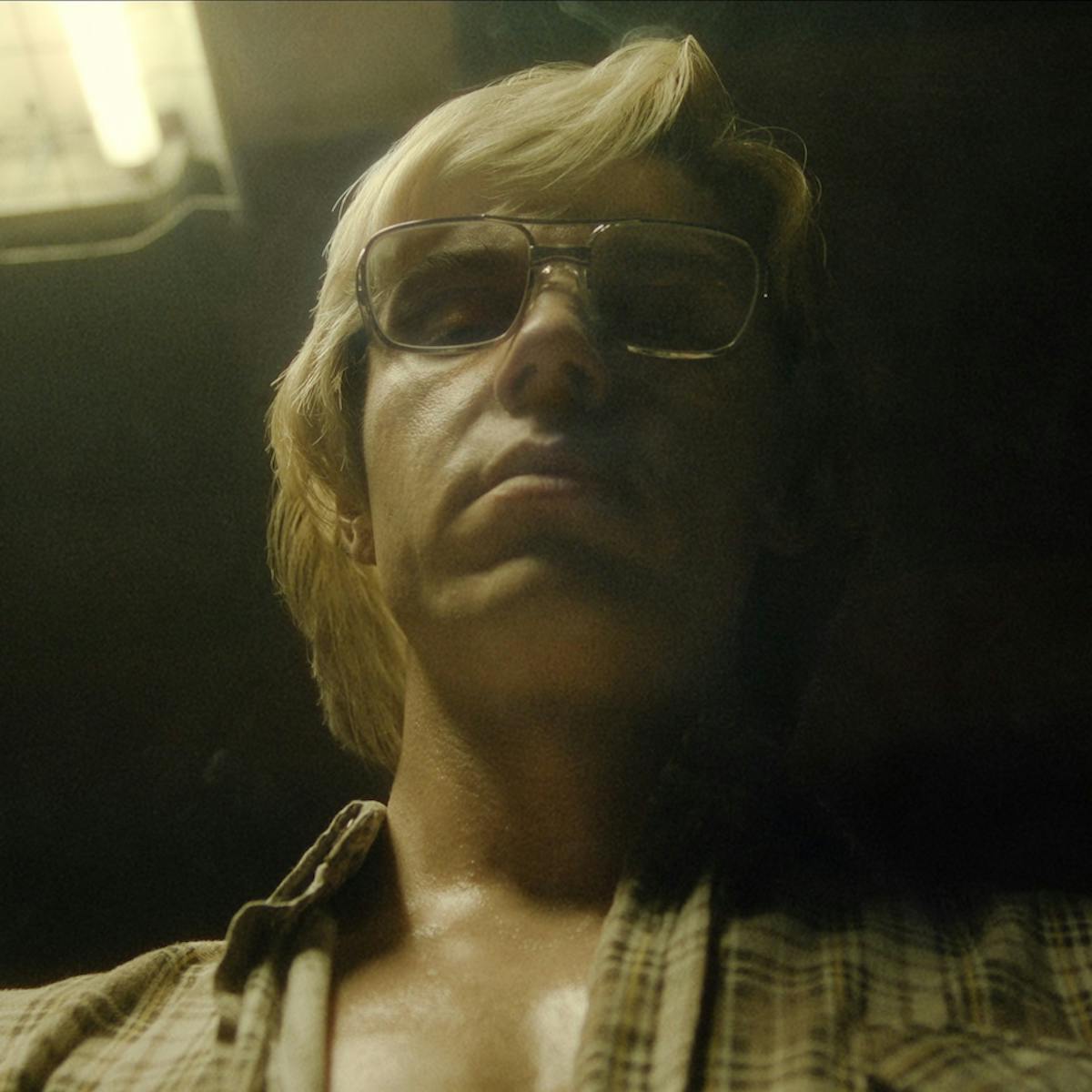 Jeffrey Dahmer (Evan Peters) is sweaty and looks menacing. His face is lit by a yellow light.