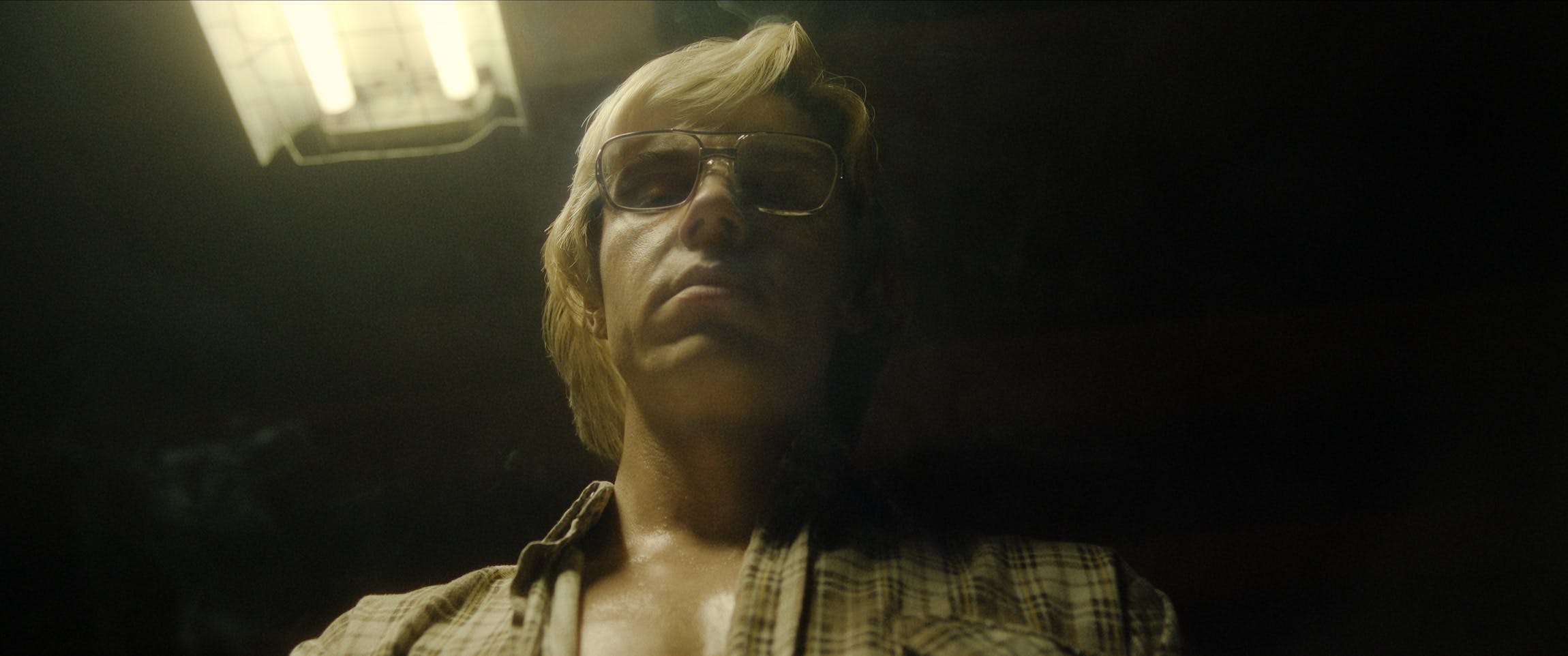 Jeffrey Dahmer (Evan Peters) is sweaty and looks menacing. His face is lit by a yellow light.