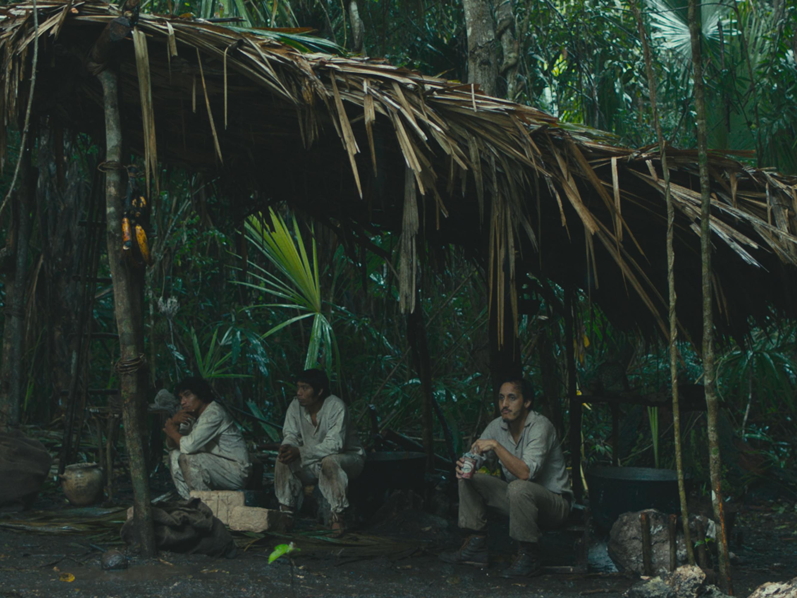 Three characters from Selva trágica sit underneath a palm roof in the jungle.