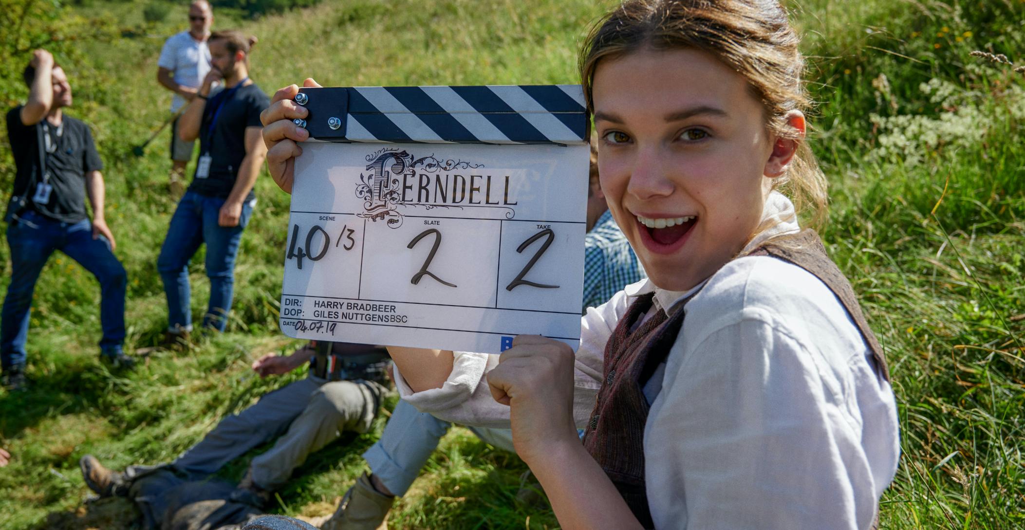 Millie Bobby Brown on set, holding a film clapper board.