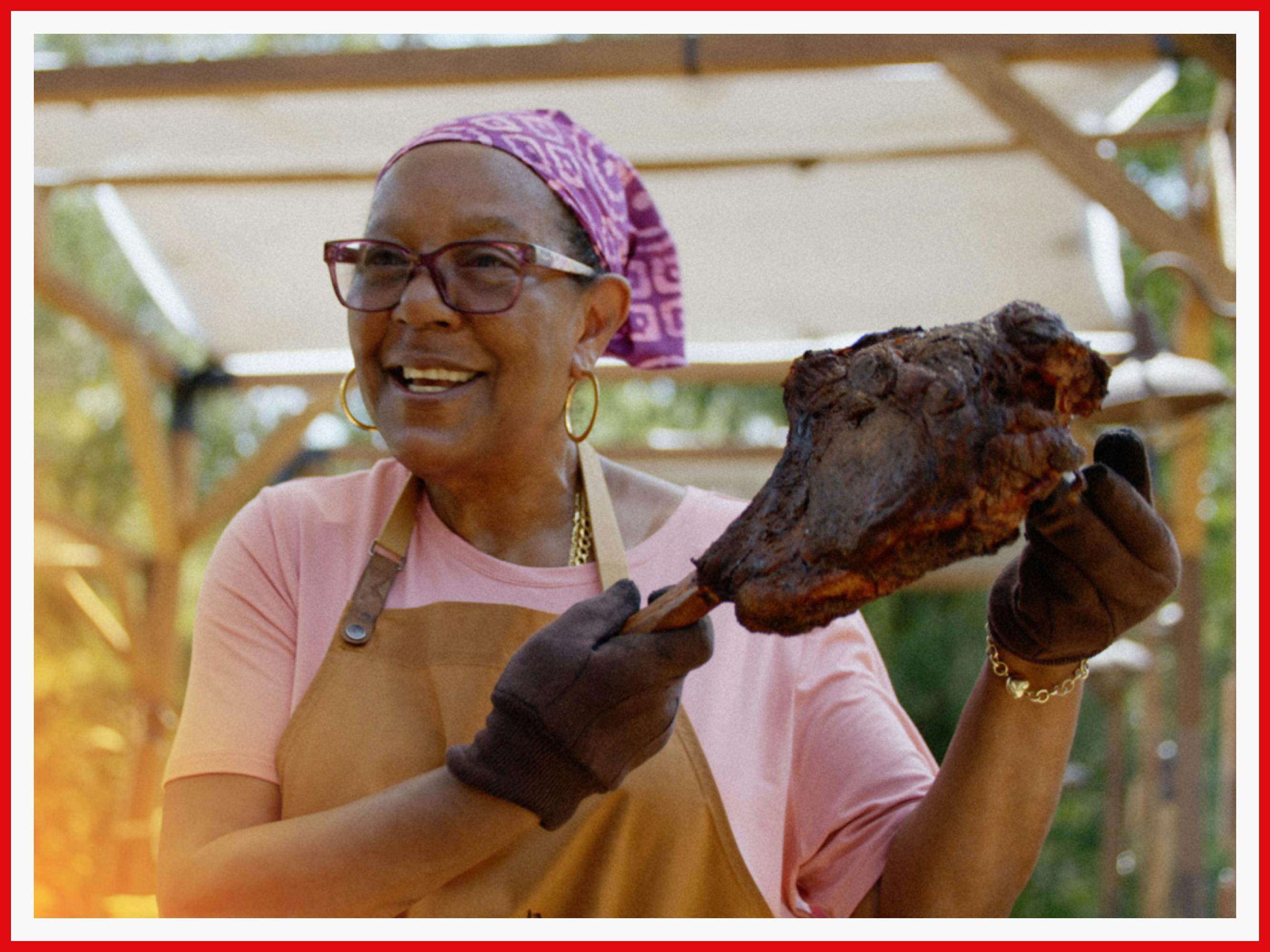 Sylvie Curry looks rightfully proud as she holds up a big cut of smoked meat. She’s color-coordinated in all pink.