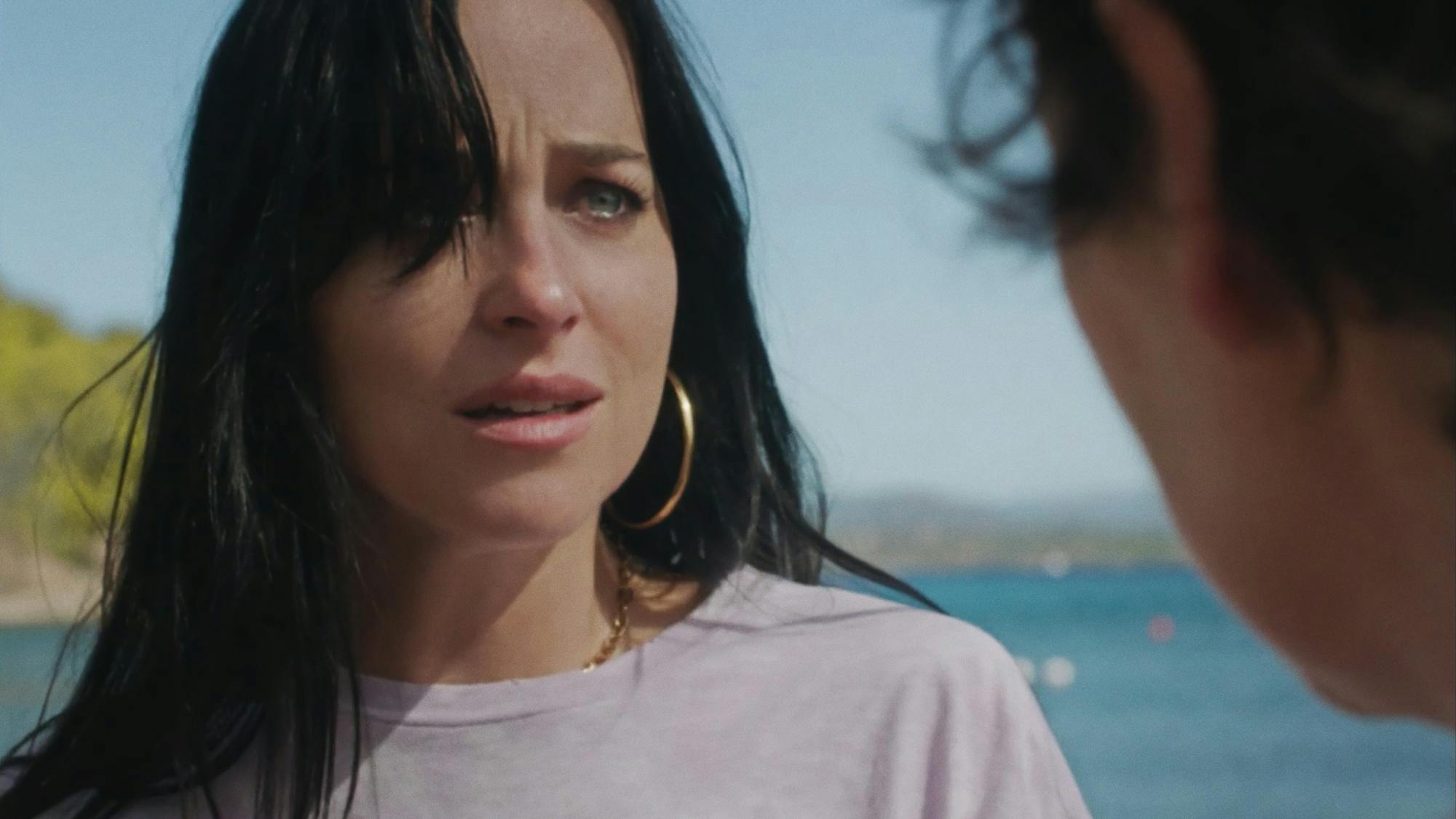 Dakota Johnson looks afraid and frantic in a white t-shirt and big hoops. She stares desperately at Olivia Colman.