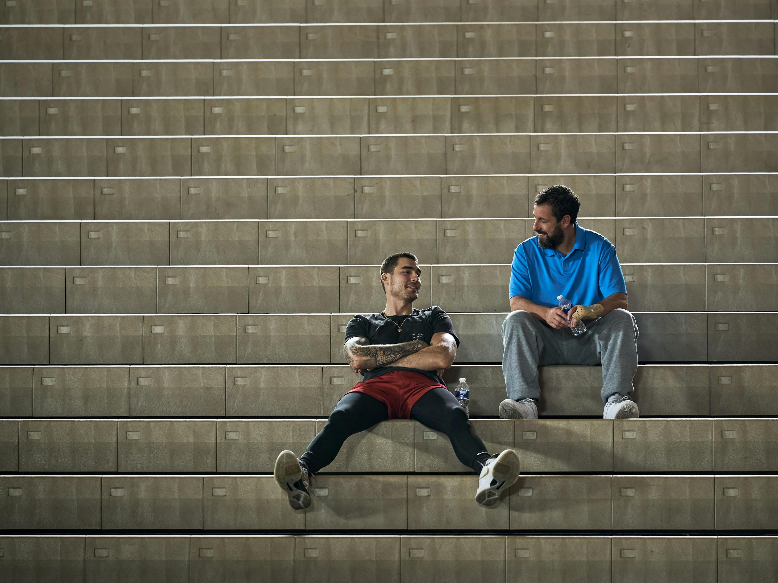 Bo Cruz (Juancho Hernangómez) and Stanley Sugarman (Adam Sandler) sit on the steps together. 