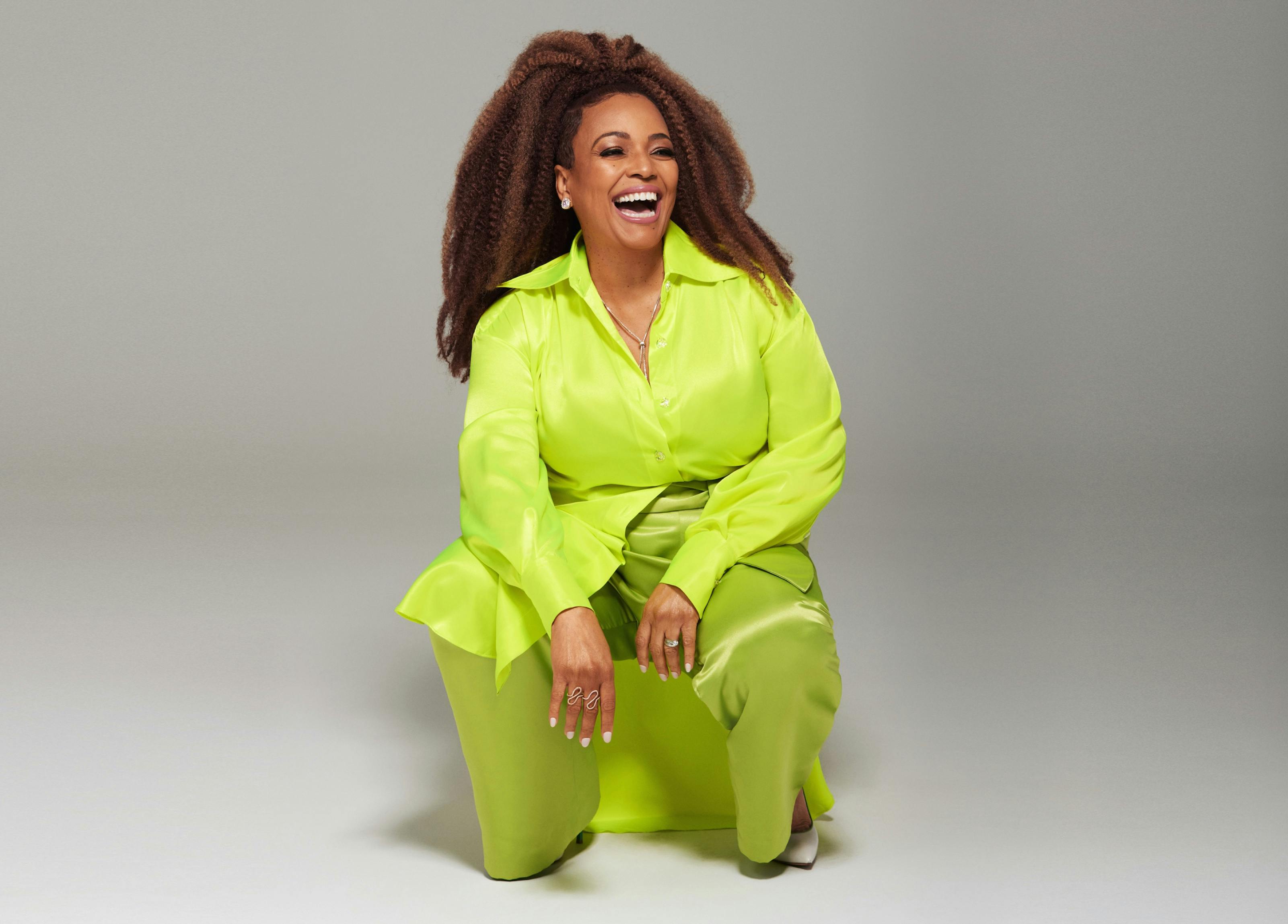 Kim Fields wears a bright green neon suit the color of a tennis ball. Her hair is long and her smile huge — she laughs at something off screen. Her hands glitter with jewelry. 