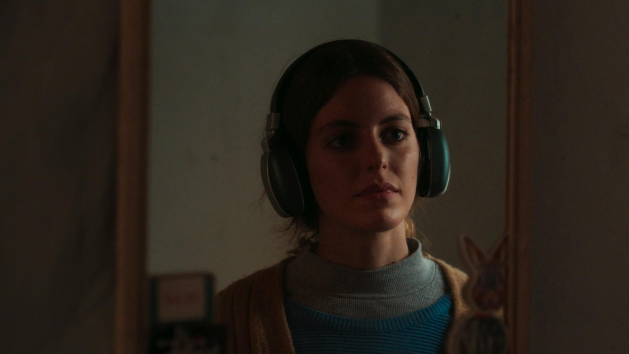 Hayrünnisa looks in the mirror, wearing a large pair of green headphones.