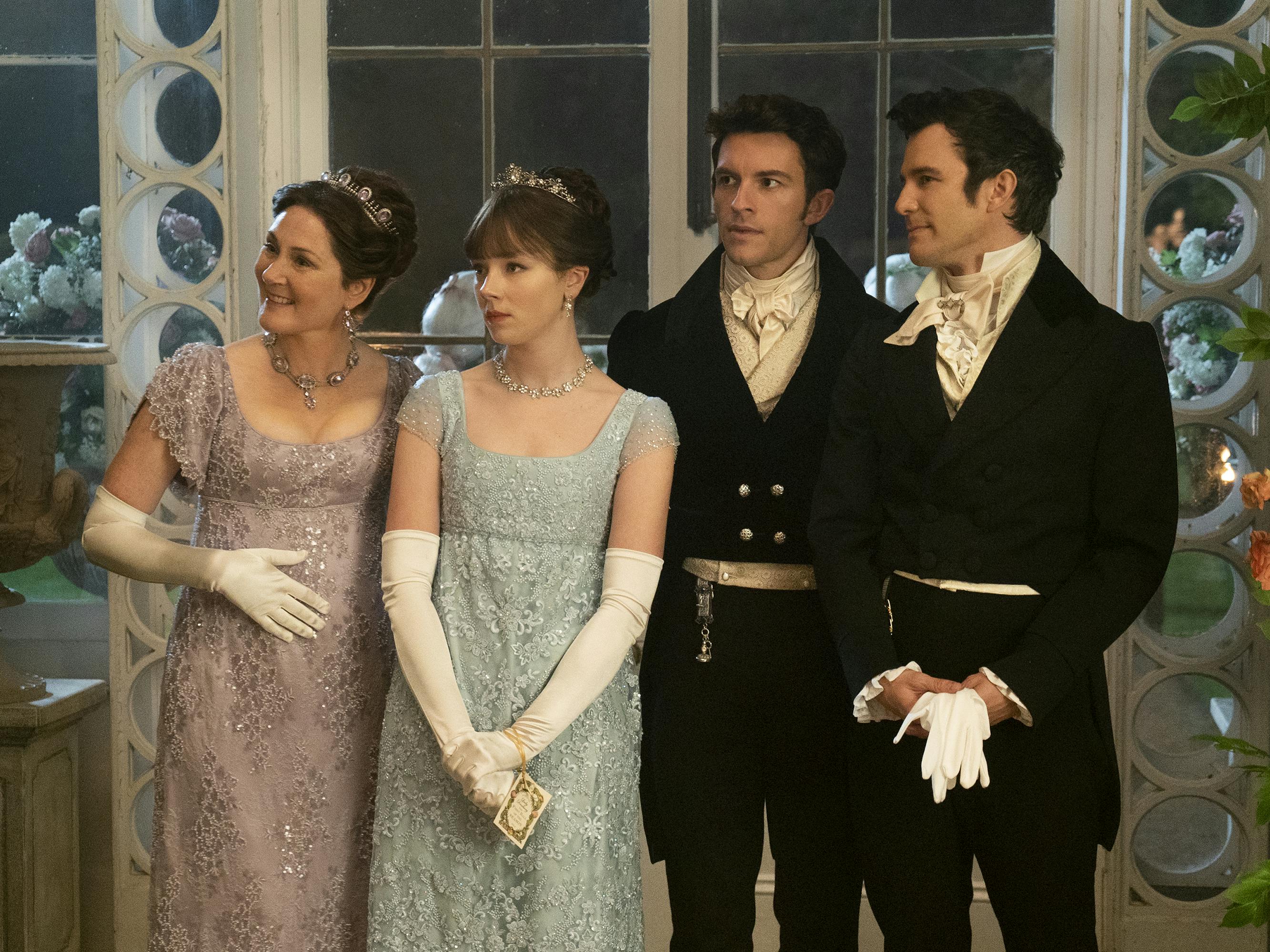 Ruth Gemmell, Claudia Jessie, Jonathan Bailey, and Luke Thompson stand together in formal wear. Gemmell wears a purple dress and long white gloves. Jessie wears a blue dress and white gloves. The two boys wears black suits and white bowties.