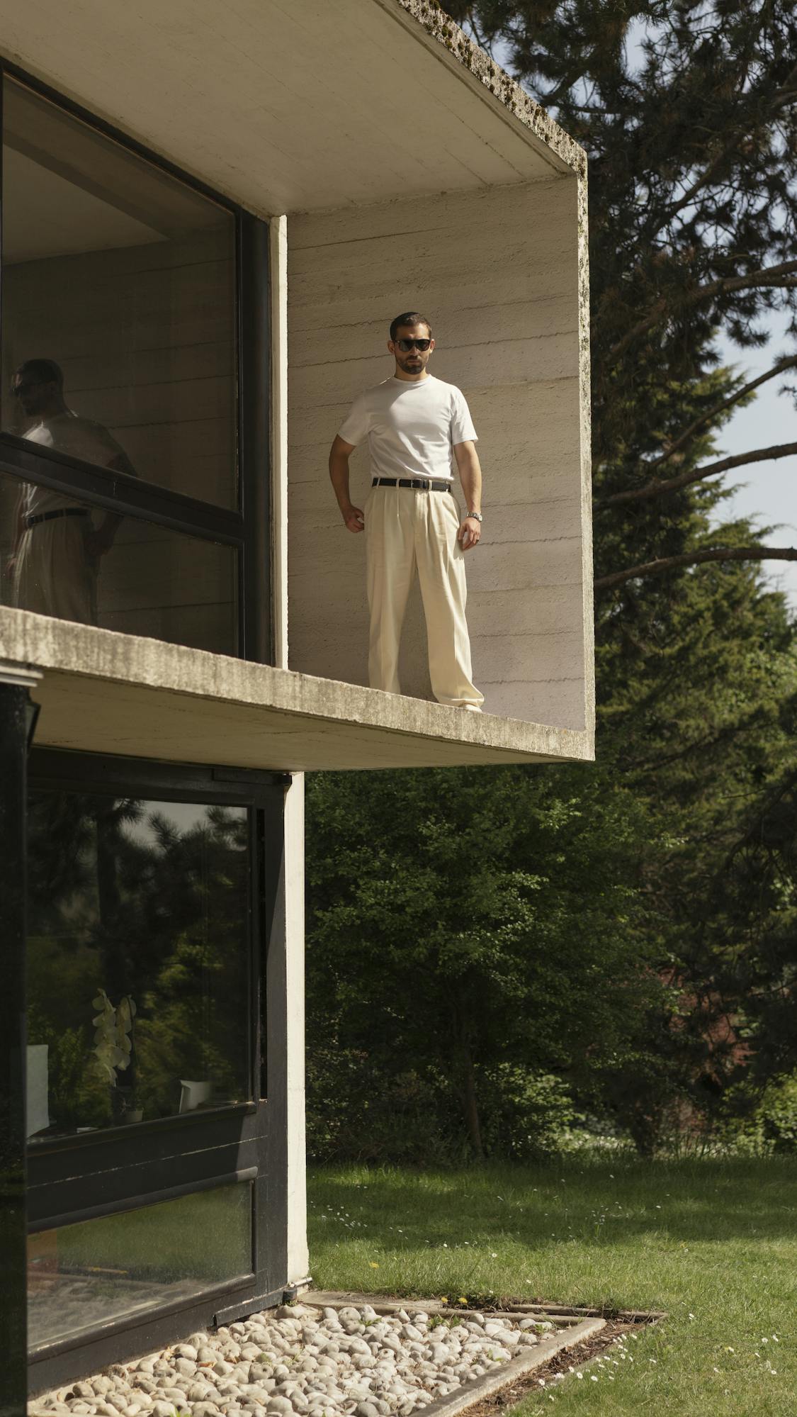 Dali Benssalah stands on a porch at a modern house wearing sunglasses, khakis and a white T-shirt.
