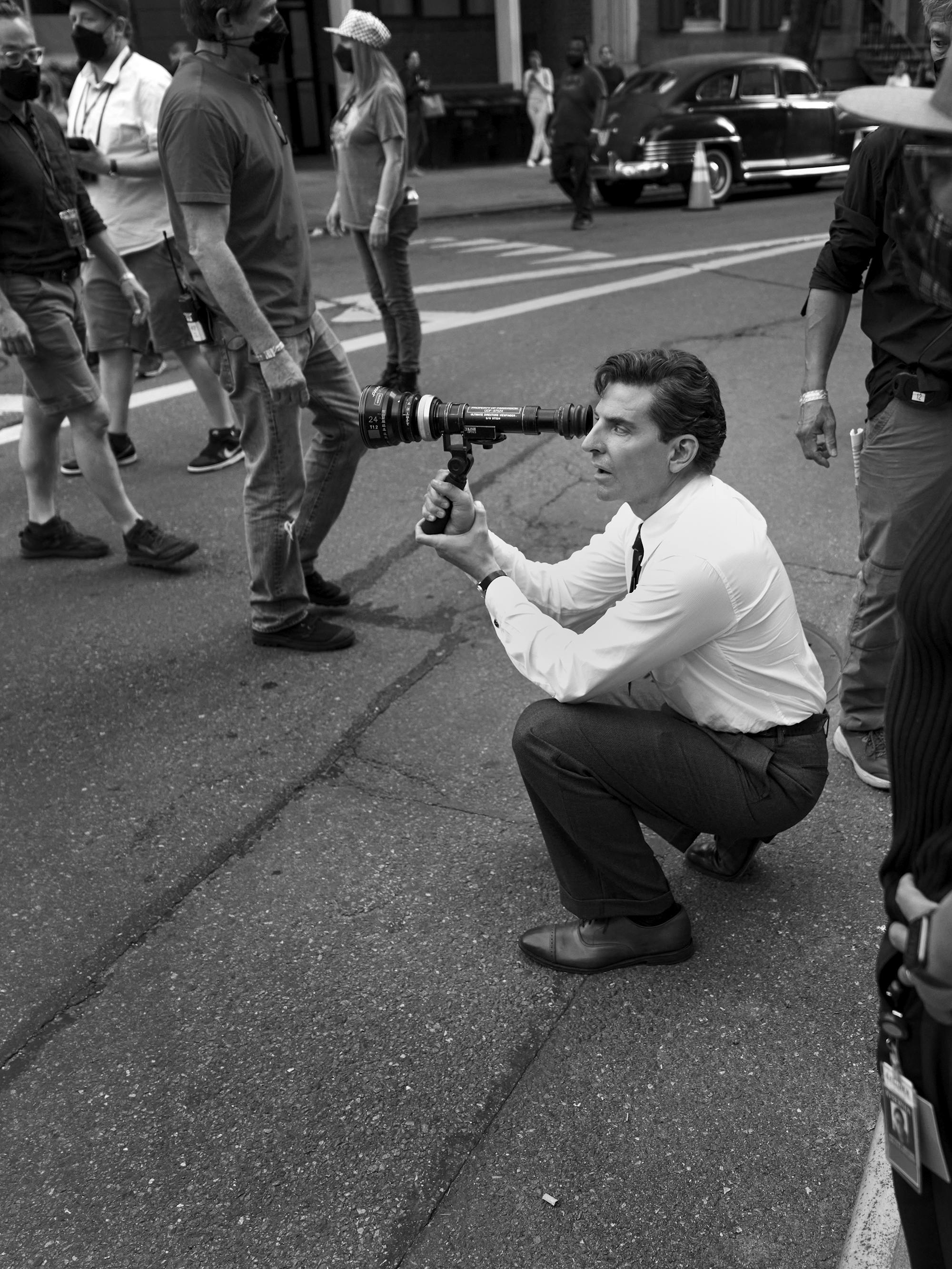 Bradley Cooper, in full costume, kneels on the street and looks into a lens.