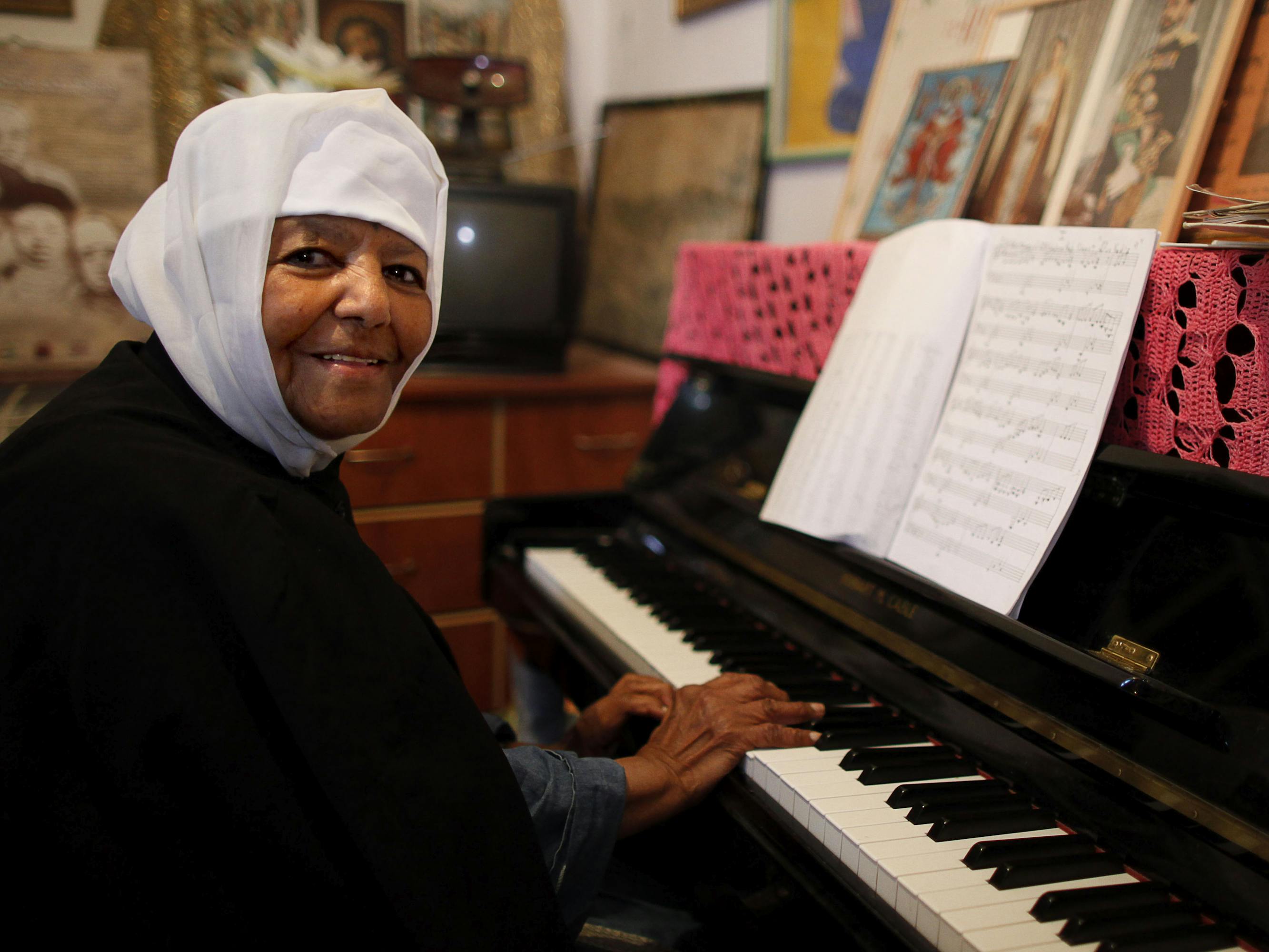Emahoy Tsegué-Maryam Guèbrou sits at a piano in a black and white nun habit.