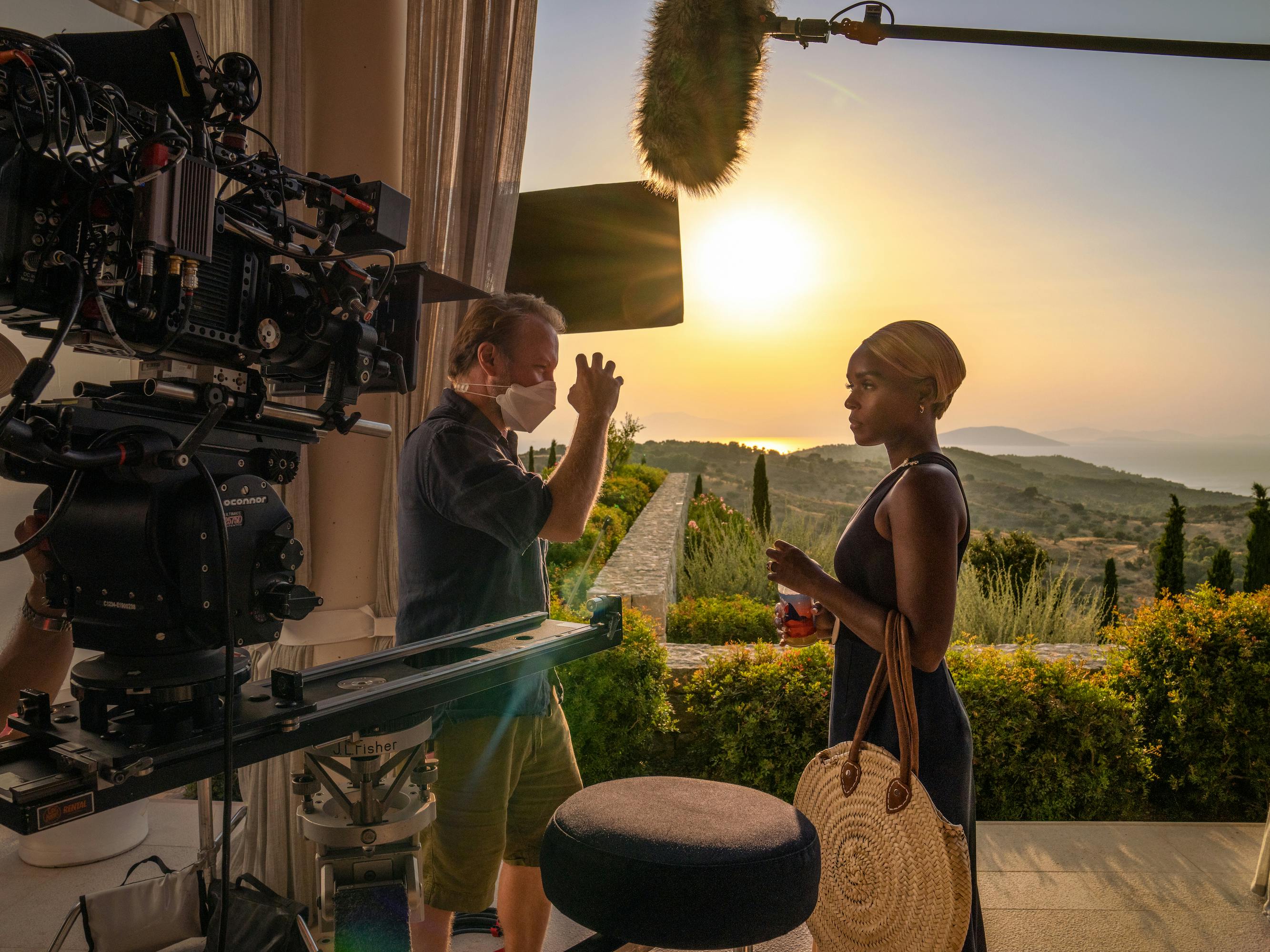Rian Johnson and Janelle Monae stand near a gorgeous green lawn lit by a huge sun. Camera gear looms in the left side.
