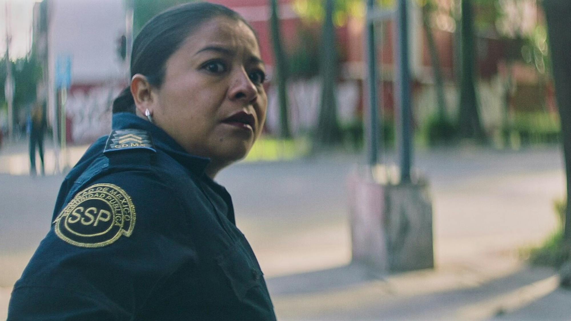 Mónica del Carmen wears her uniform and looks scared as she stands in an outdoor street.