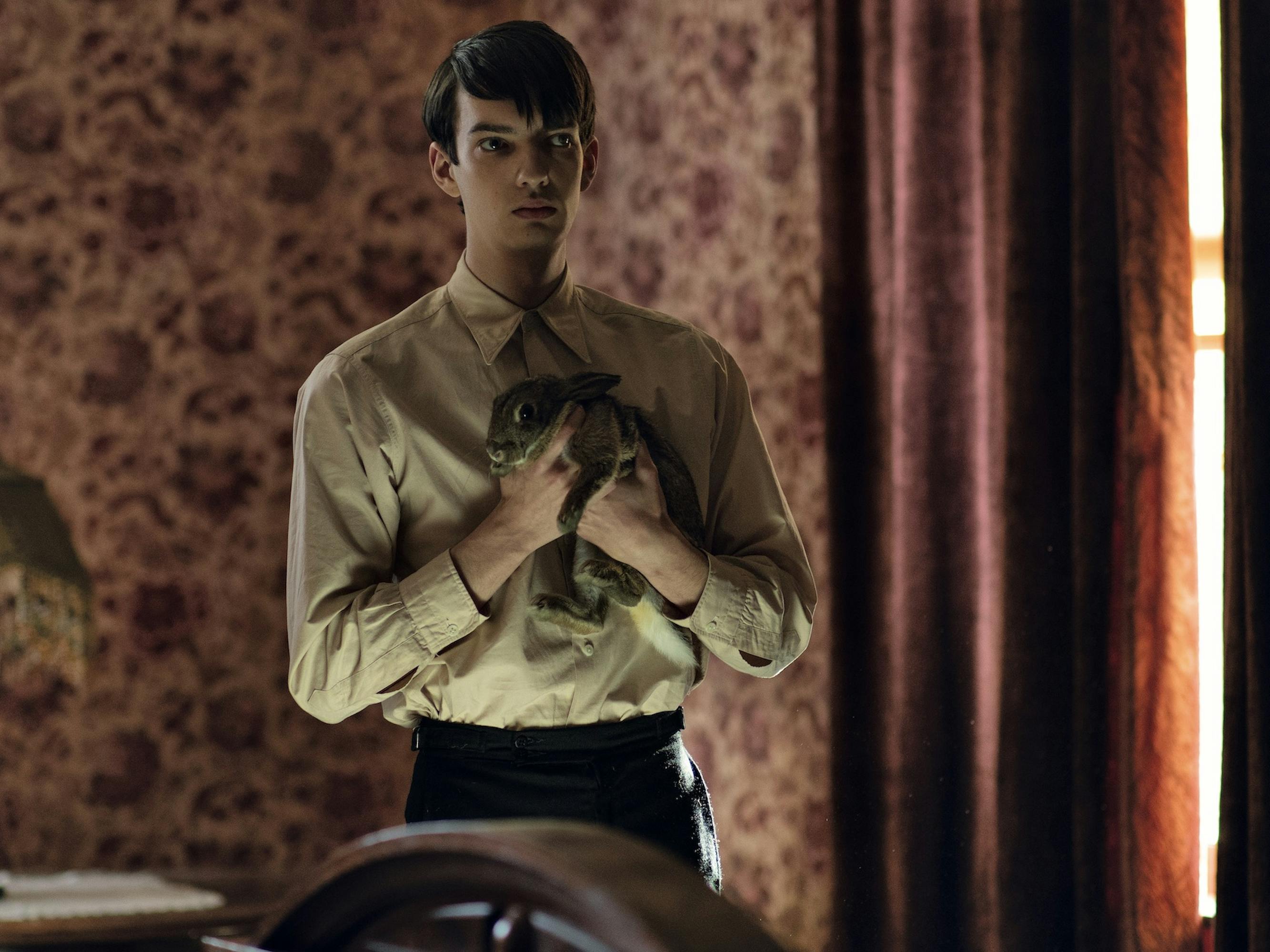 Peter Gordon (Kodi Smit-McPhee) clutches a bunny to his chest. He wears a white shirt and black pants. Behind him is a maroon flowered wallpaper and drapes.