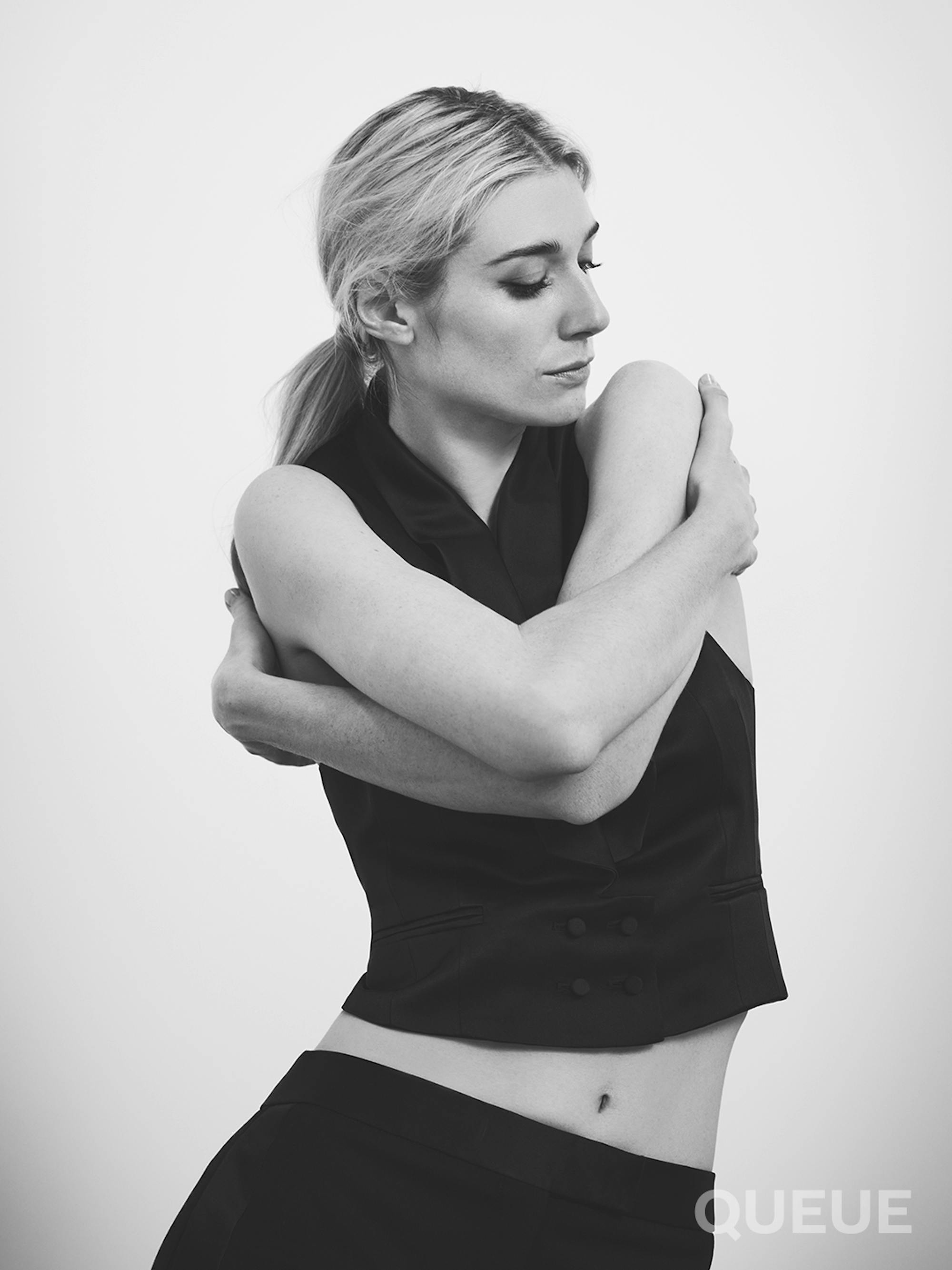 Elizabeth Debicki wears a black tank top and black bottoms and hugs herself.