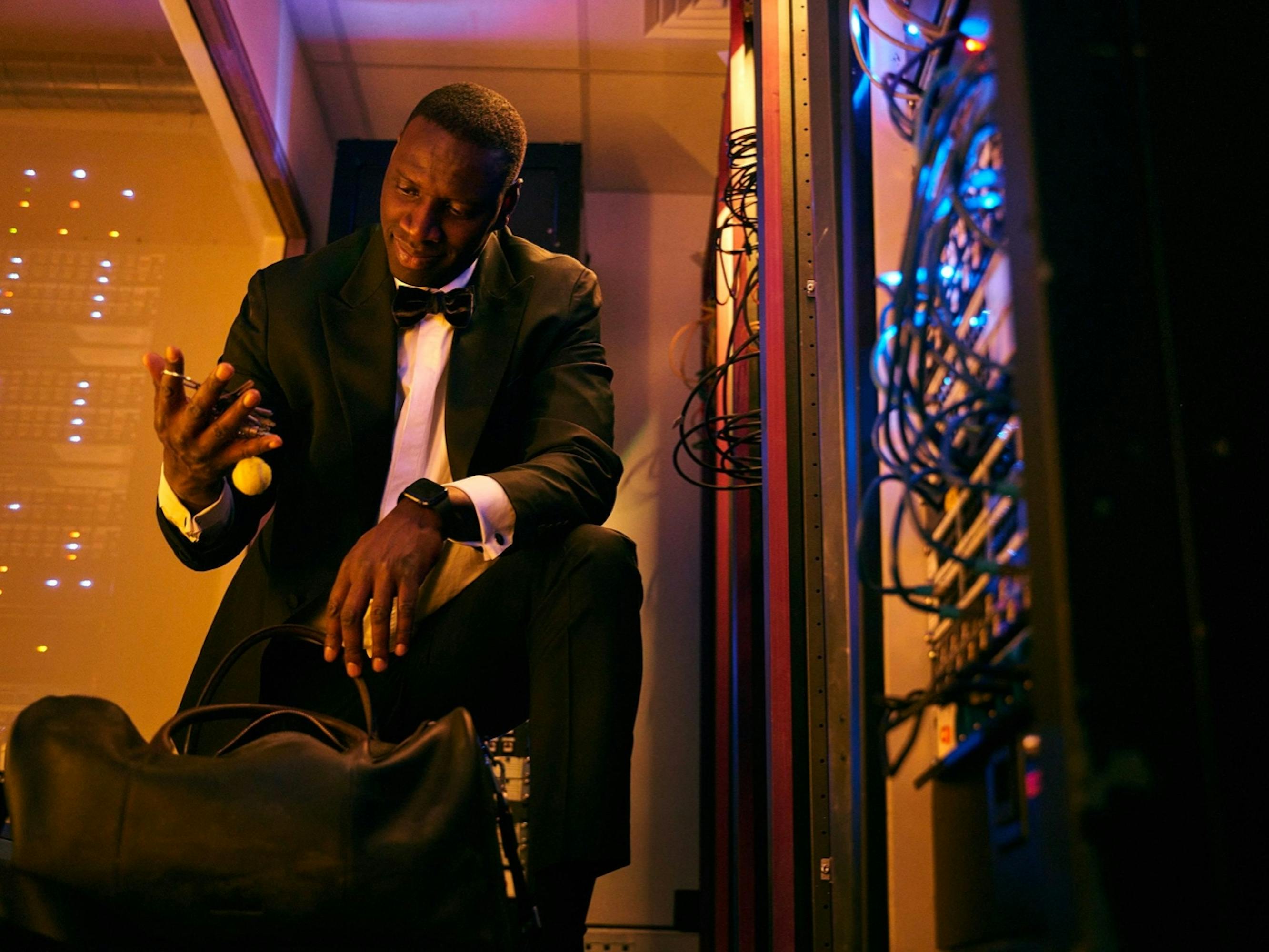 Assane Diop (Omar Sy) looks dashing in a black tux and bowtie as he crouches over a mysterious duffel in a room filled with wires.