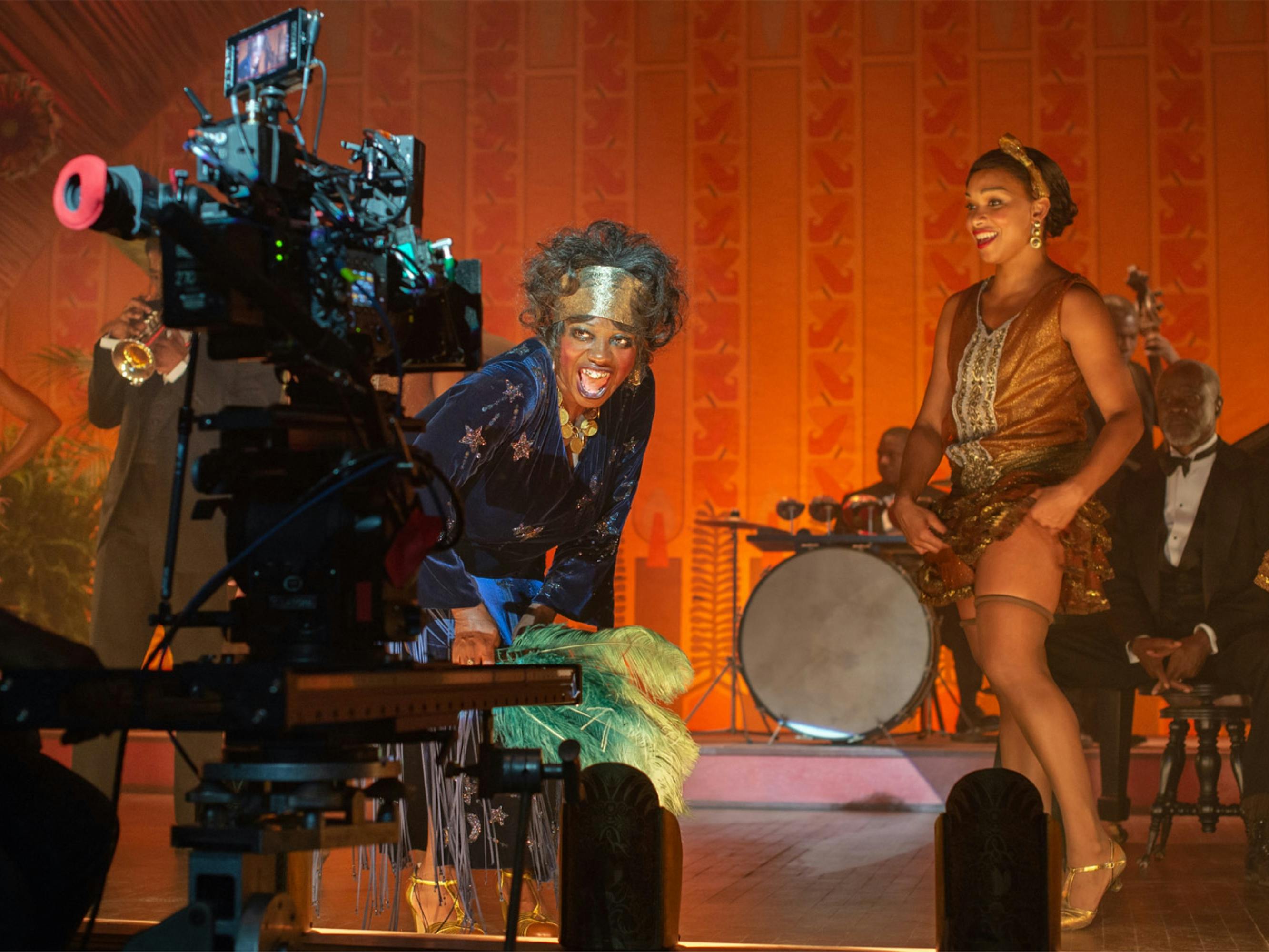 Viola Davis leans into a camera with a provocative, playful look as she shoots this tent show scene from Ma Rainey’s Black Bottom. She is surrounded by actors in heels and short skirts, playing dancers.