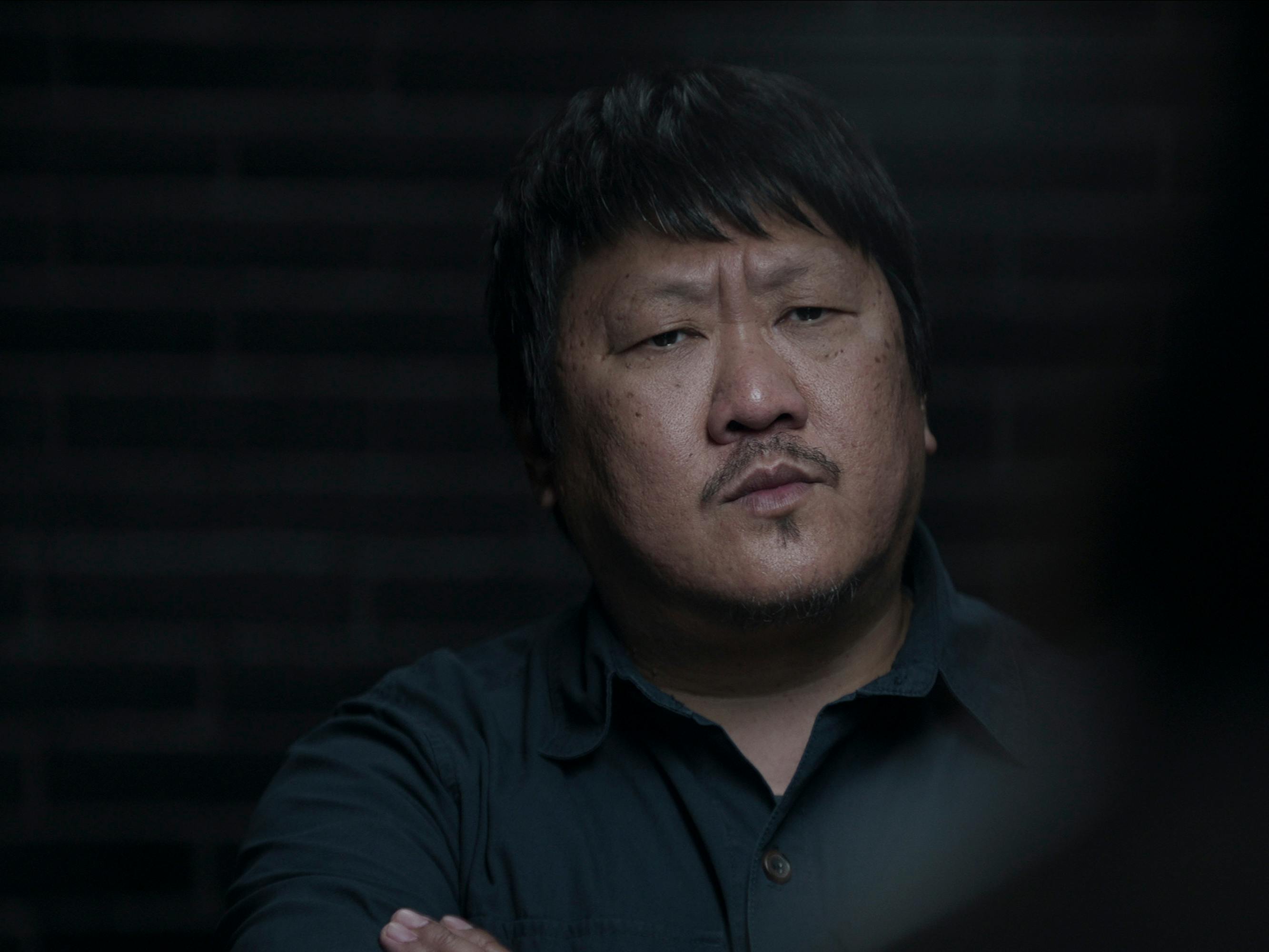 Da Shi (Benedict Wong) wears a navy shirt and crosses his arms in the dark.