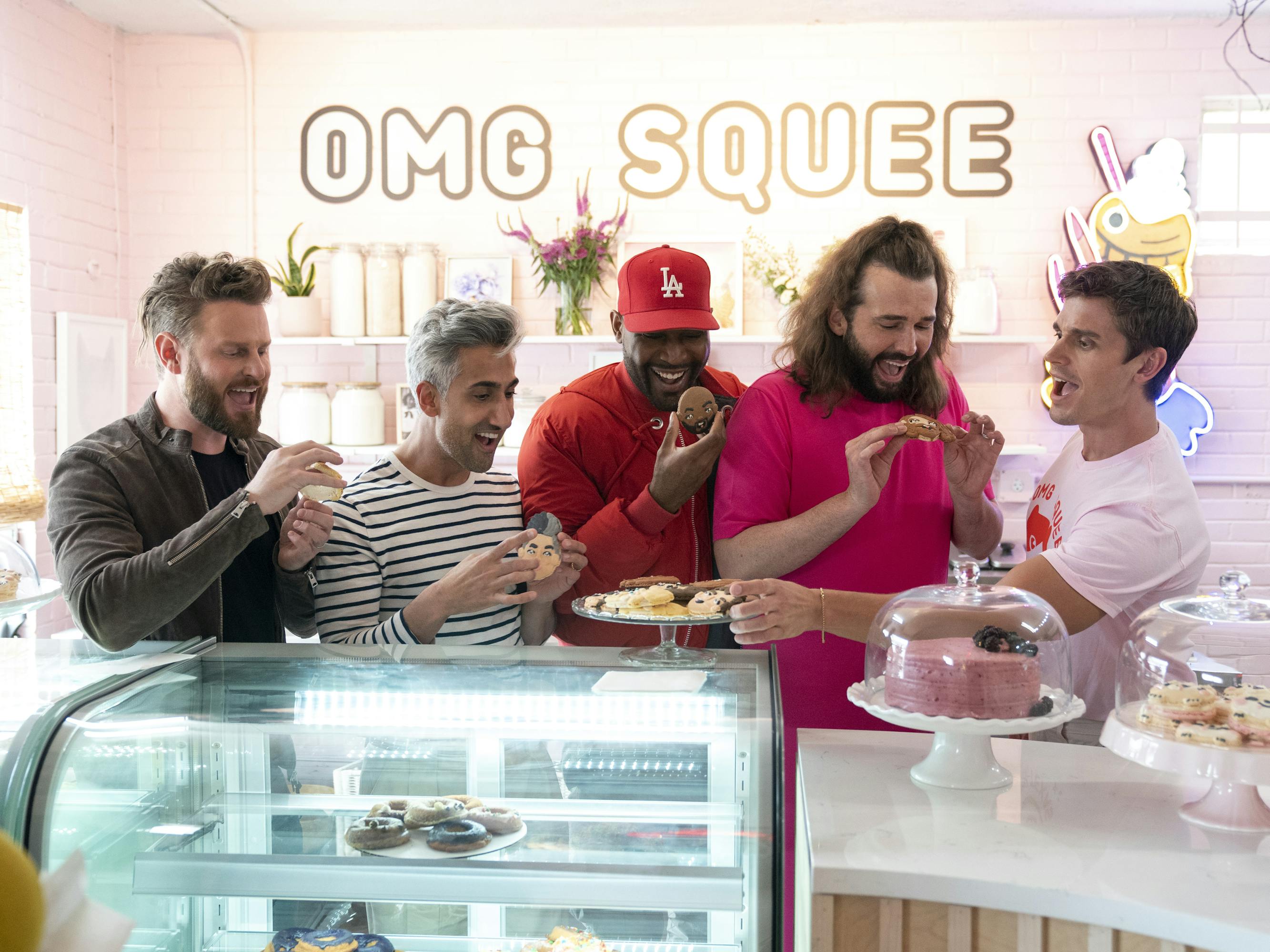 The Fab Five sample cookies with their faces on them in a shop that is brightly lit, with flowers on a shelf, and 'OMG SQUEE' in gold writing.