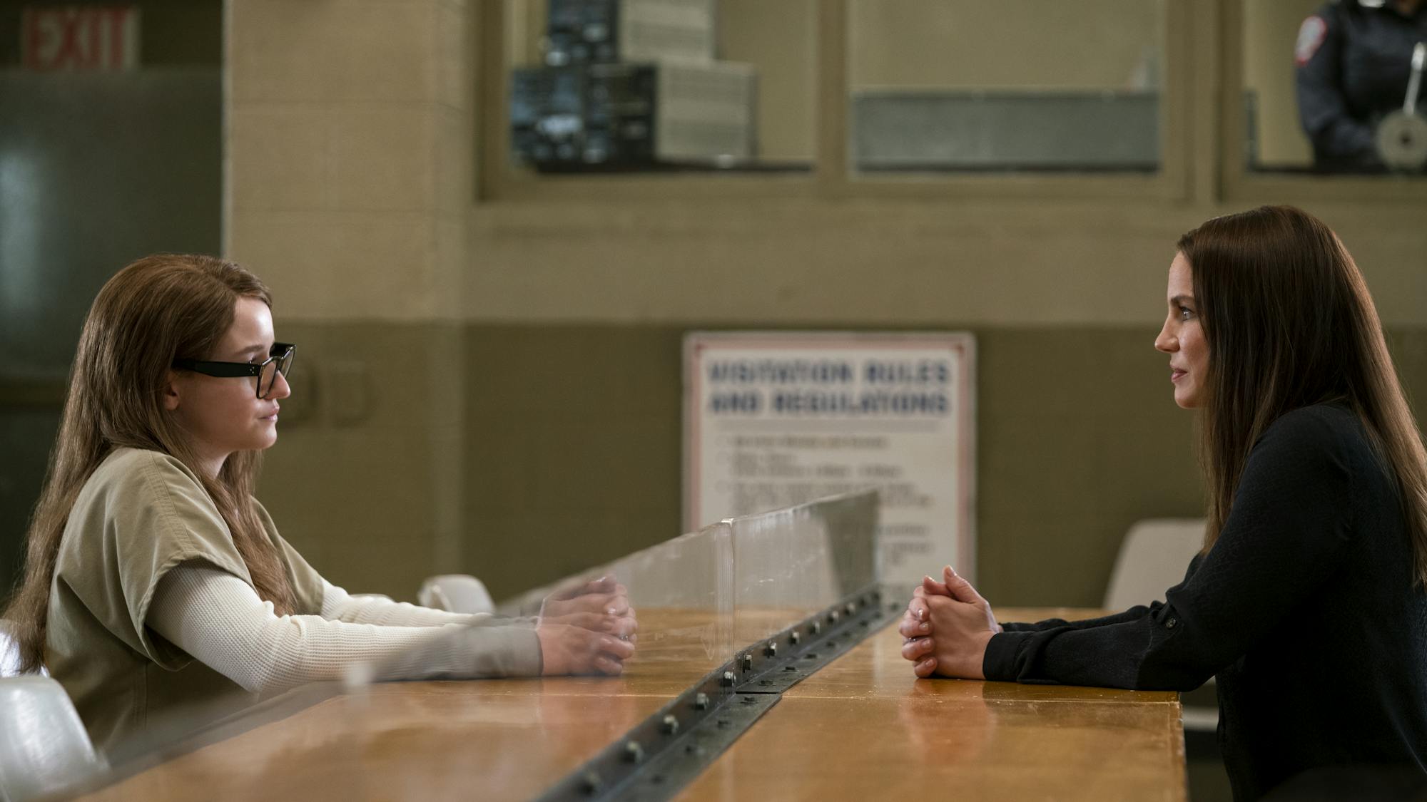 Julia Garner as Anna Delvy (Sorokin) sits across from Anna Chlumsky as Vivian Kent in a visitor's room at Rikers jail. 