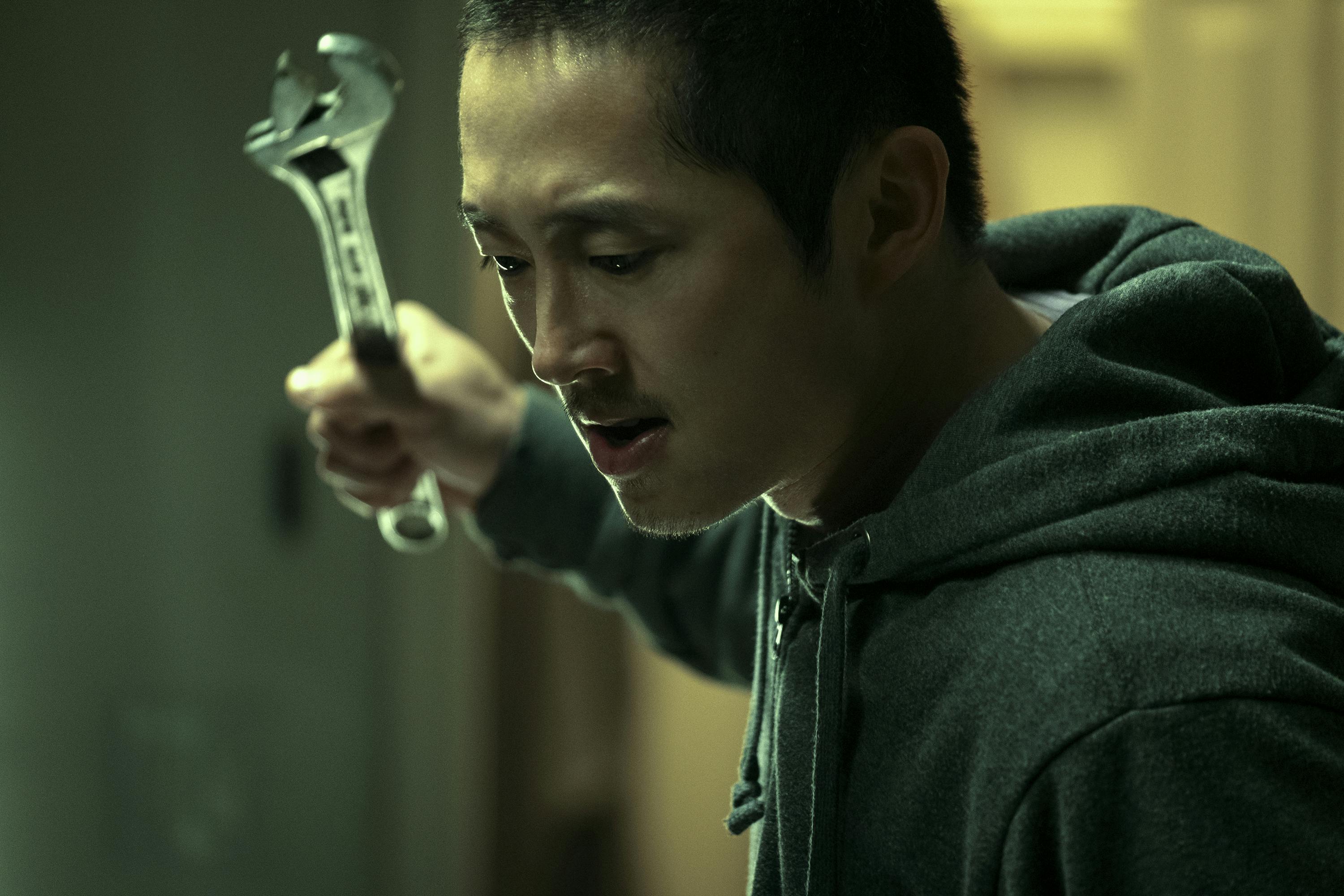 Danny (Steven Yeun) holds a wrench up, with a ferocious expression.