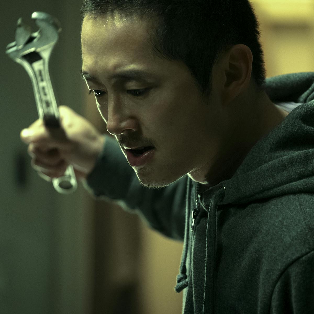 Danny (Steven Yeun) holds a wrench up, with a ferocious expression.