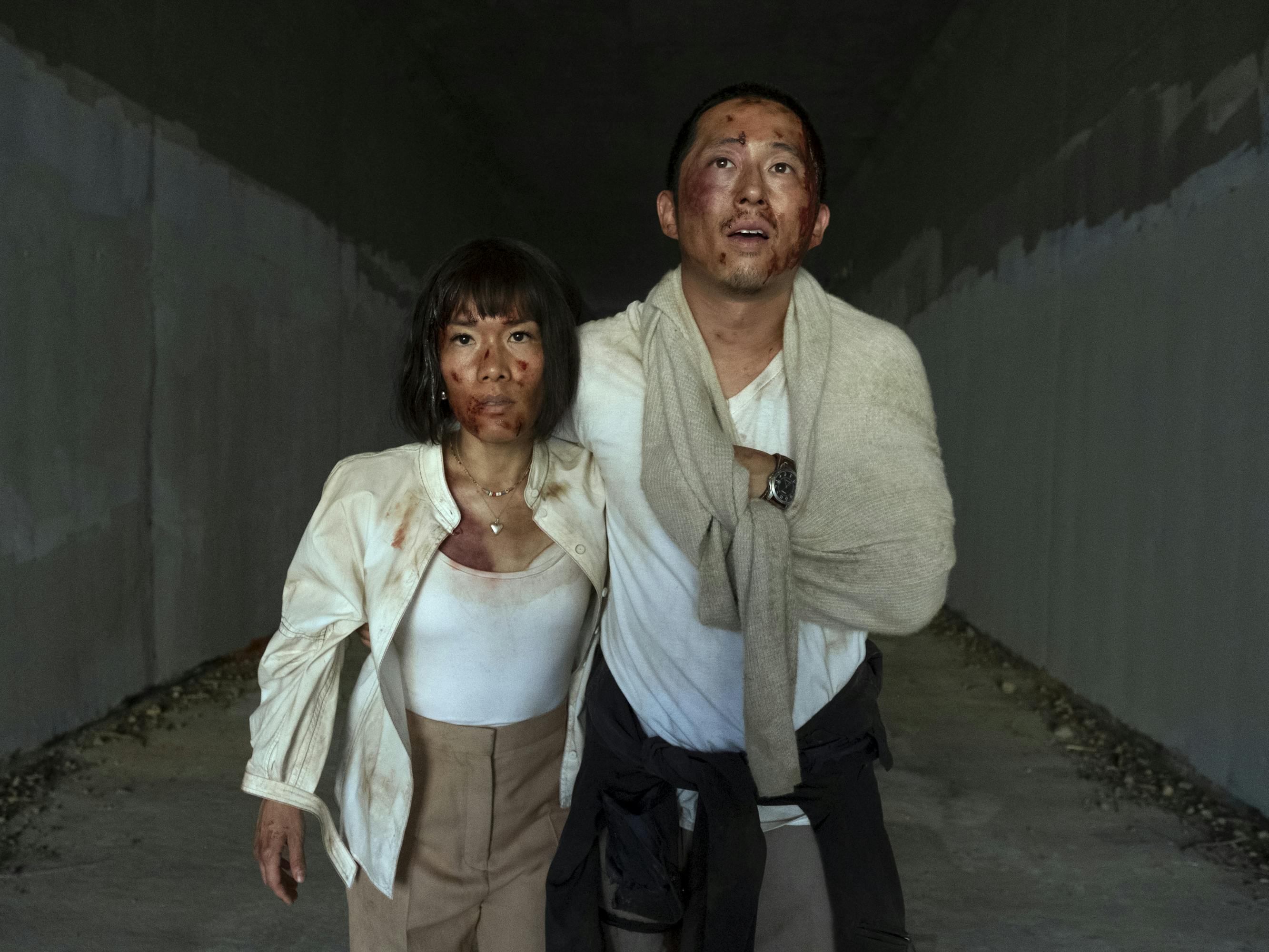 Amy (Ali Wong) and Danny (Steven Yeun) stagger through a dark tunnel, bloodied and dirty.