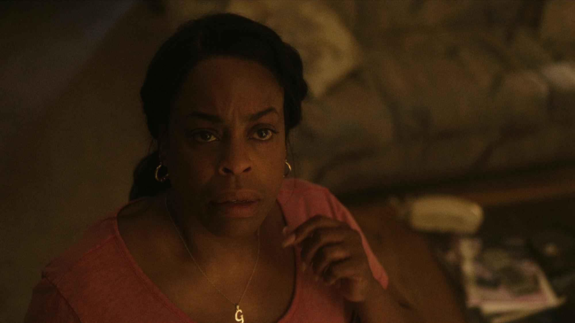 Glenda Cleveland (Niecy Nash-Betts) wears a pink top and gold necklace and looks afraid.
