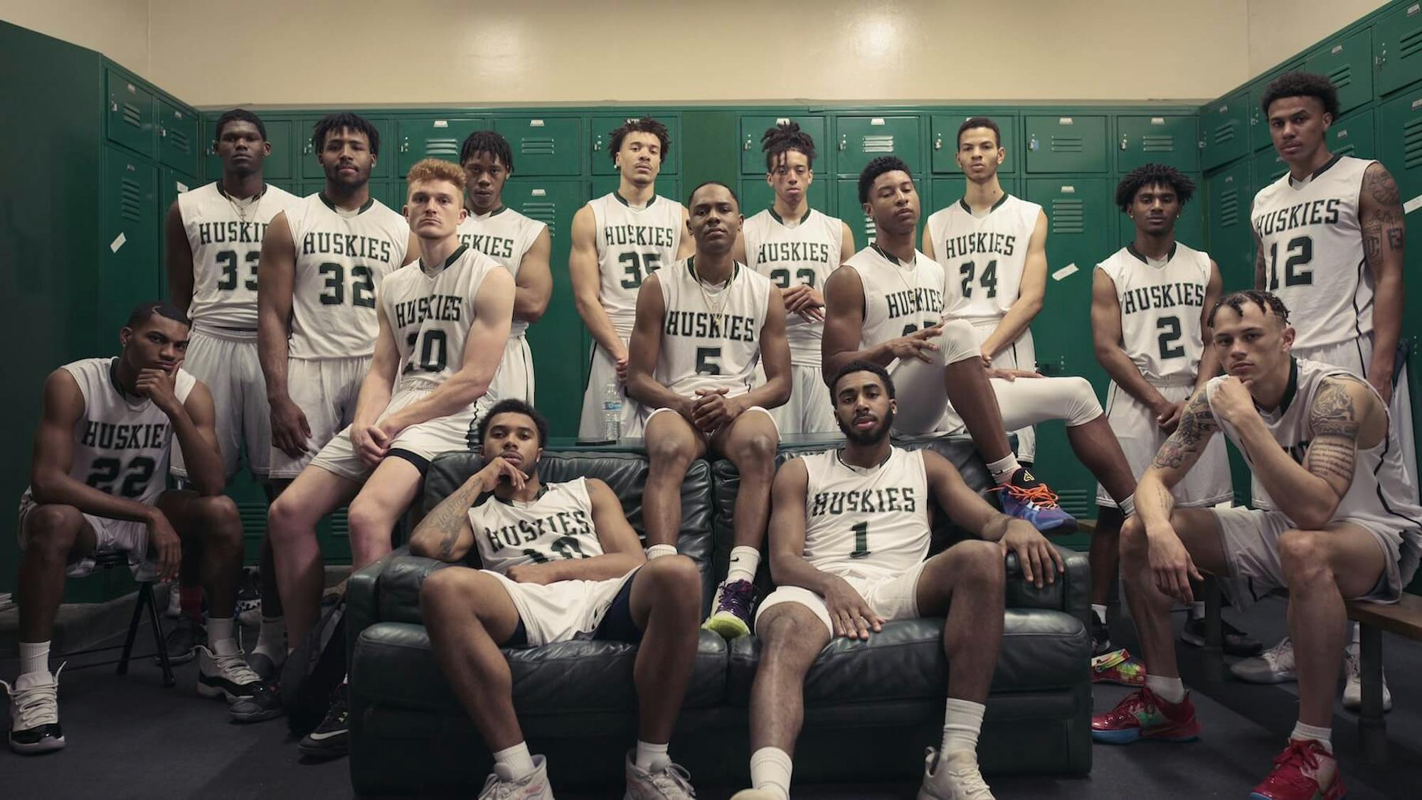 East Los Angeles College Huskies pose for a photo in their green locker room. They wear their jerseys, and look at the camera with serious expressions.